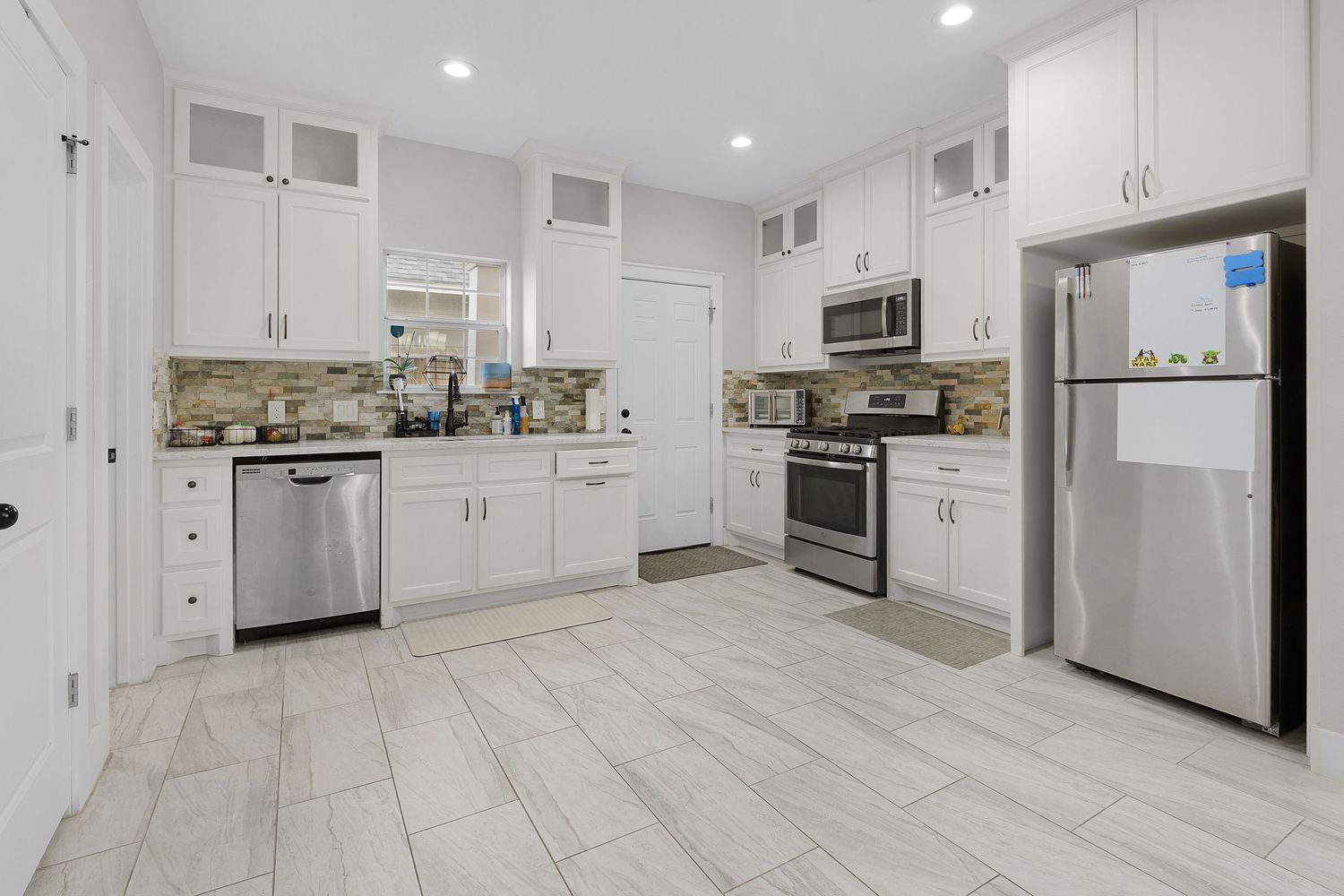Contemporary white kitchen with stainless steel appliances, tile backsplash, and light-colored flooring.