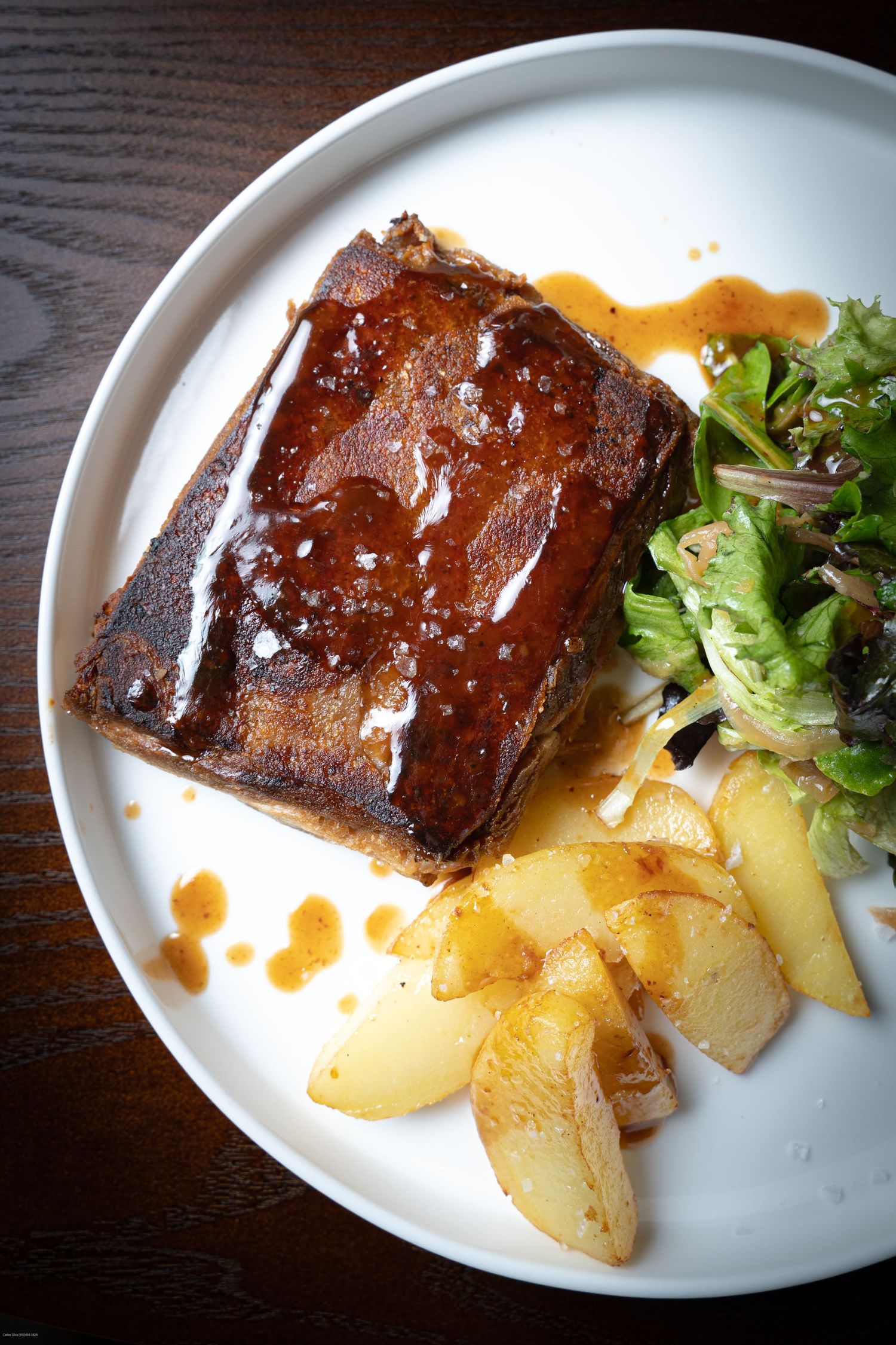 Glazed pork belly with roasted potatoes and fresh herbs served on a white plate.