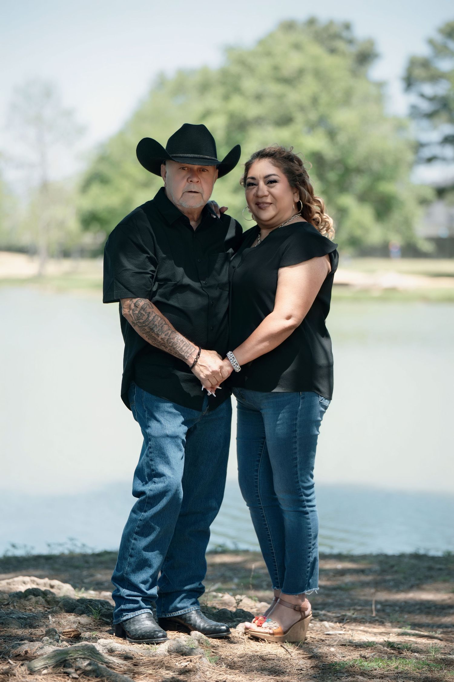 Couple in casual attire posing together by lakeside.