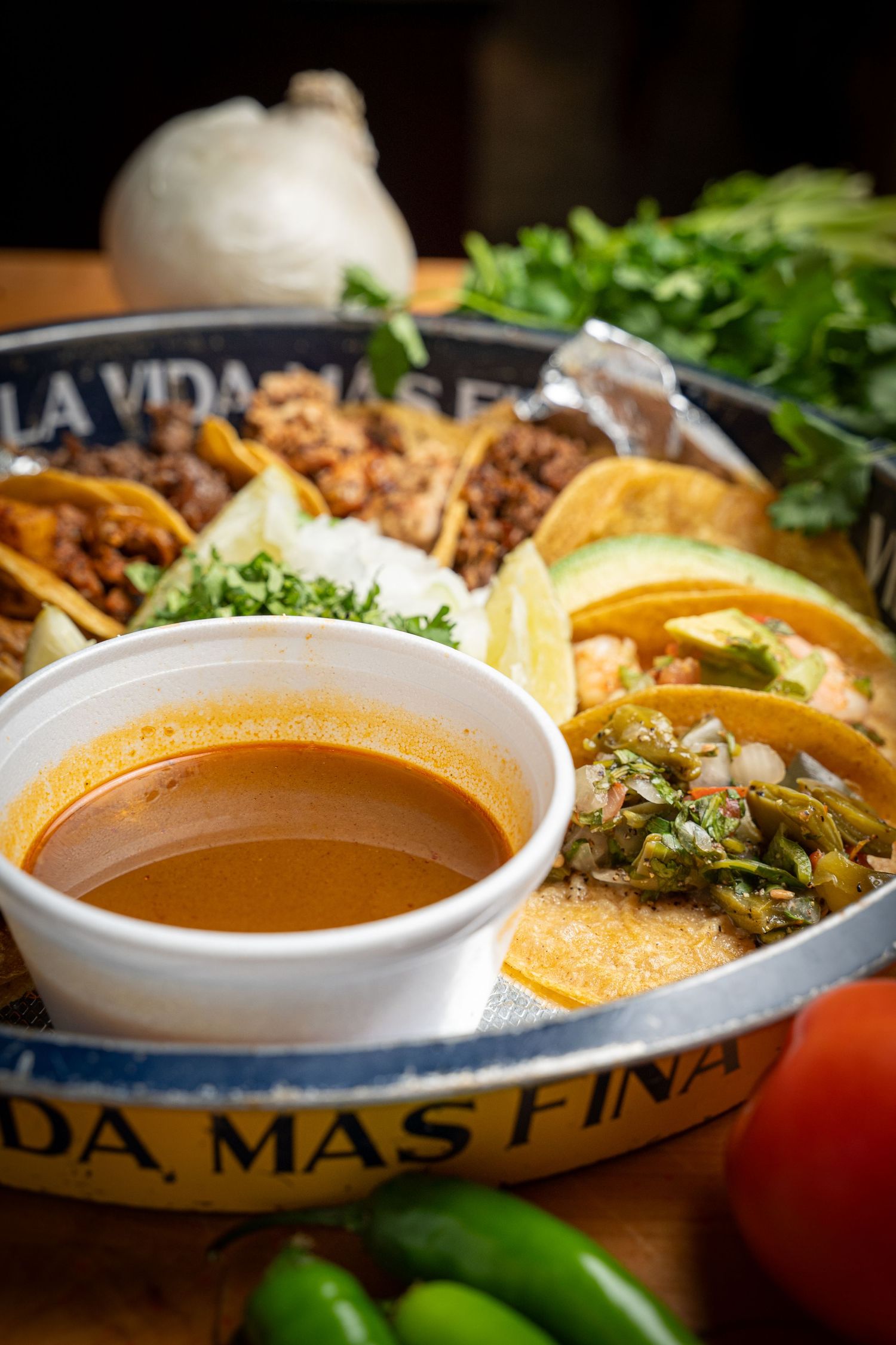 Steaming hot Mexican soup or consomme served in white bowls alongside garnishes and tortilla chips.