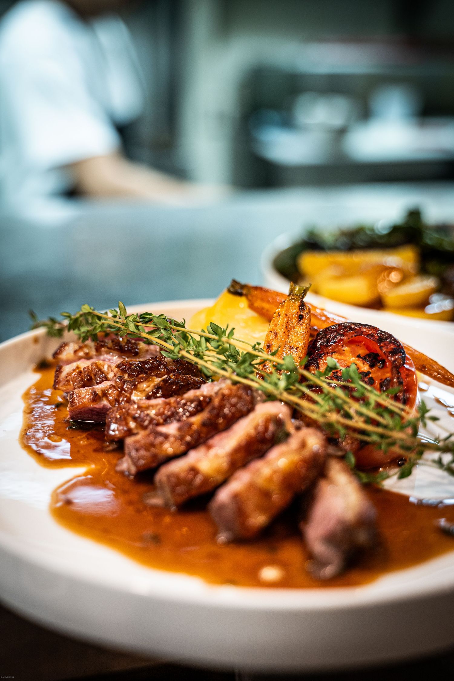 Grilled duck breast with thyme garnish served in a rich brown sauce on a white plate.