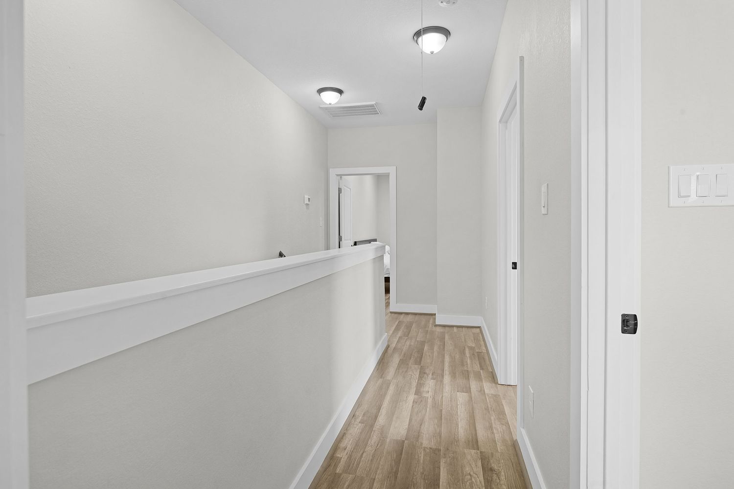 Bright hallway with white walls, light wood flooring and modern ceiling lights.