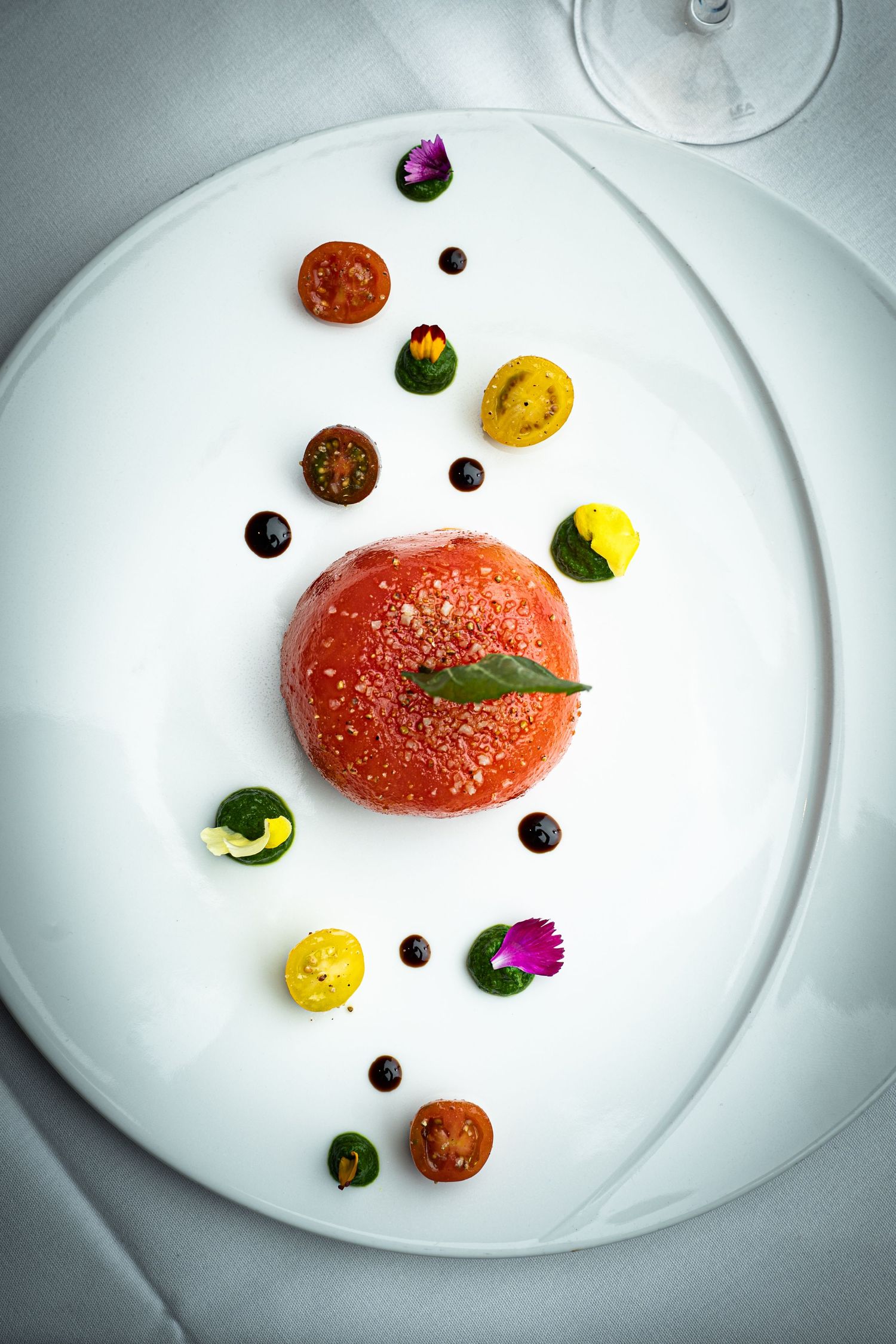 Elegant fine dining dish with tomato centerpiece, edible flowers, cherry tomatoes, and black caviar on white plate.