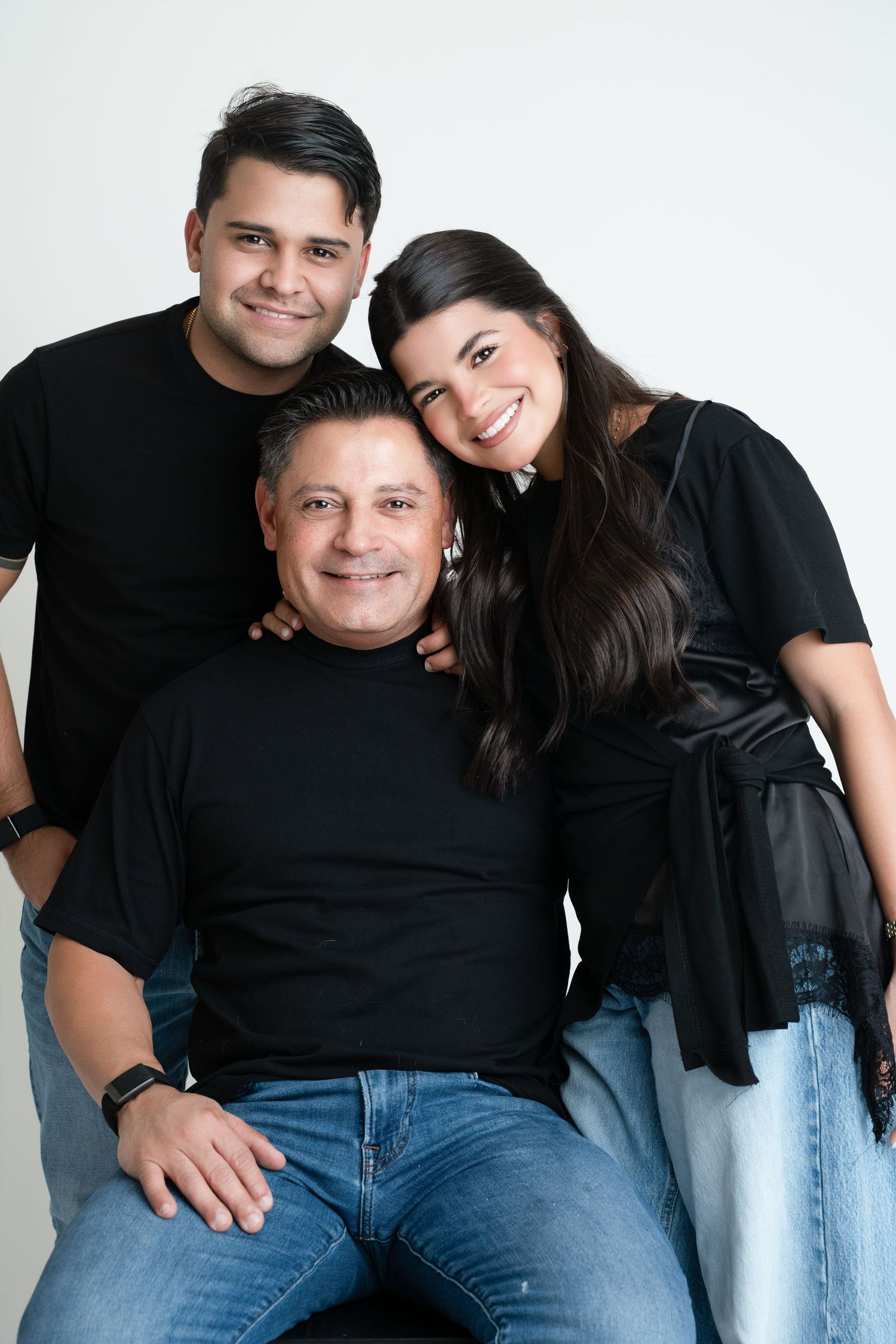 Three smiling family members in matching black tops pose together for a portrait against a white background.