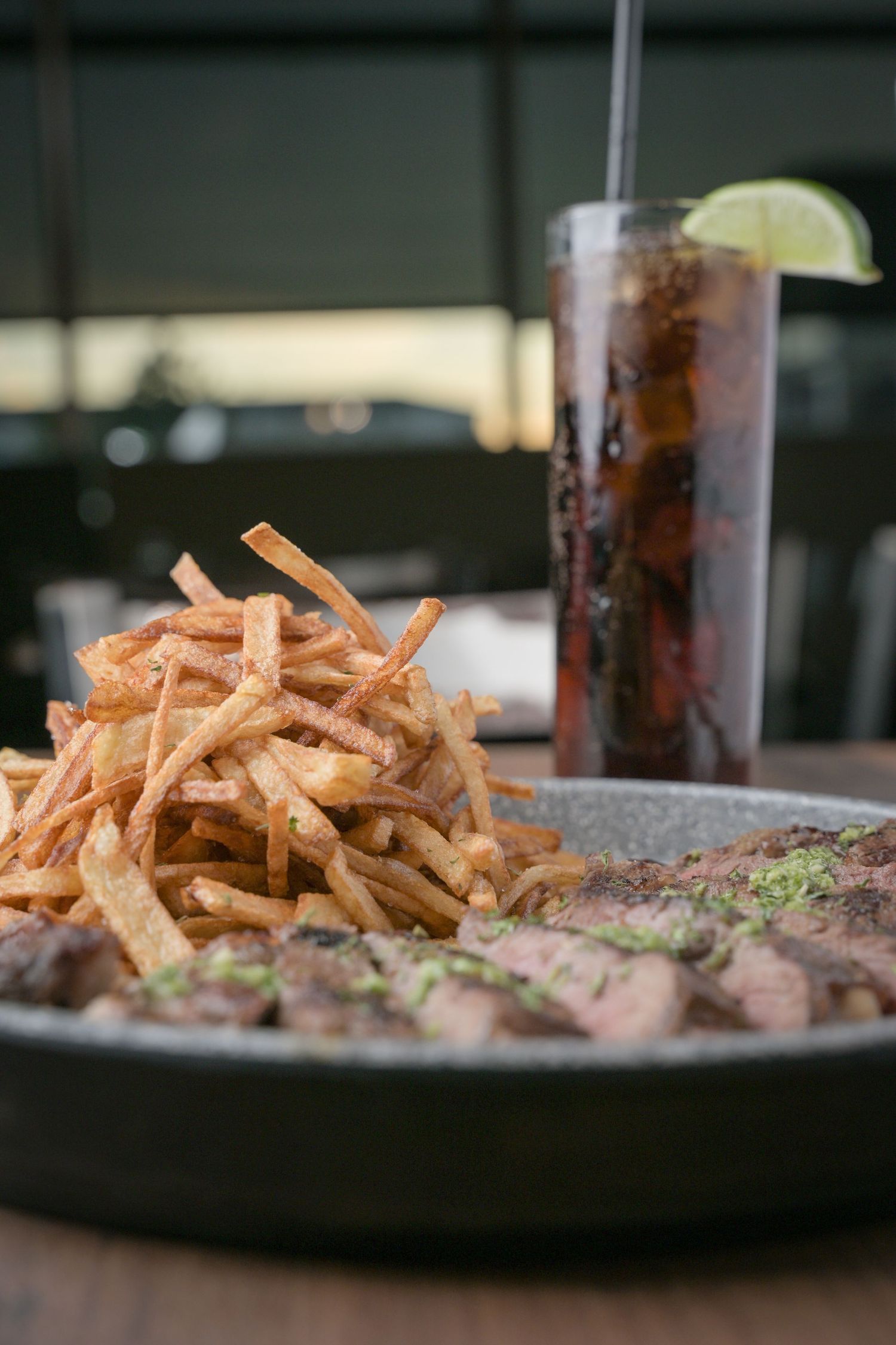 Grilled steak with crispy shoestring fries and soft drink on restaurant table.