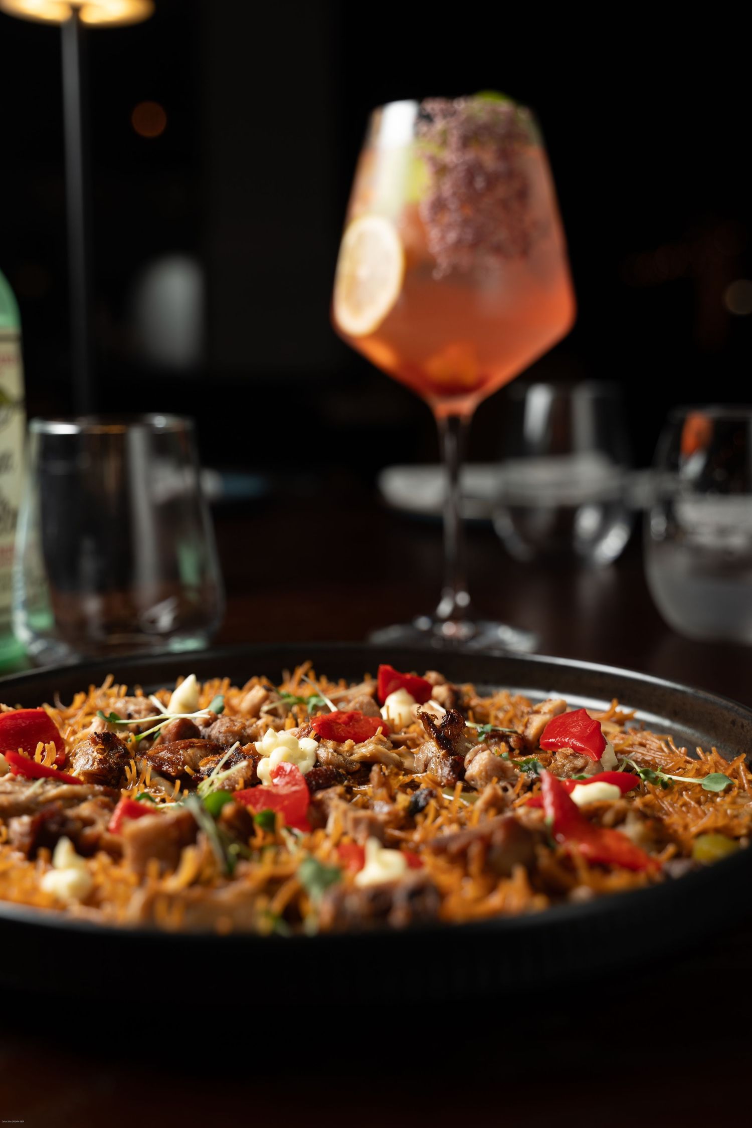 Close-up view of paella with colorful vegetables and crispy rice edges served in a traditional pan in dim lighting.