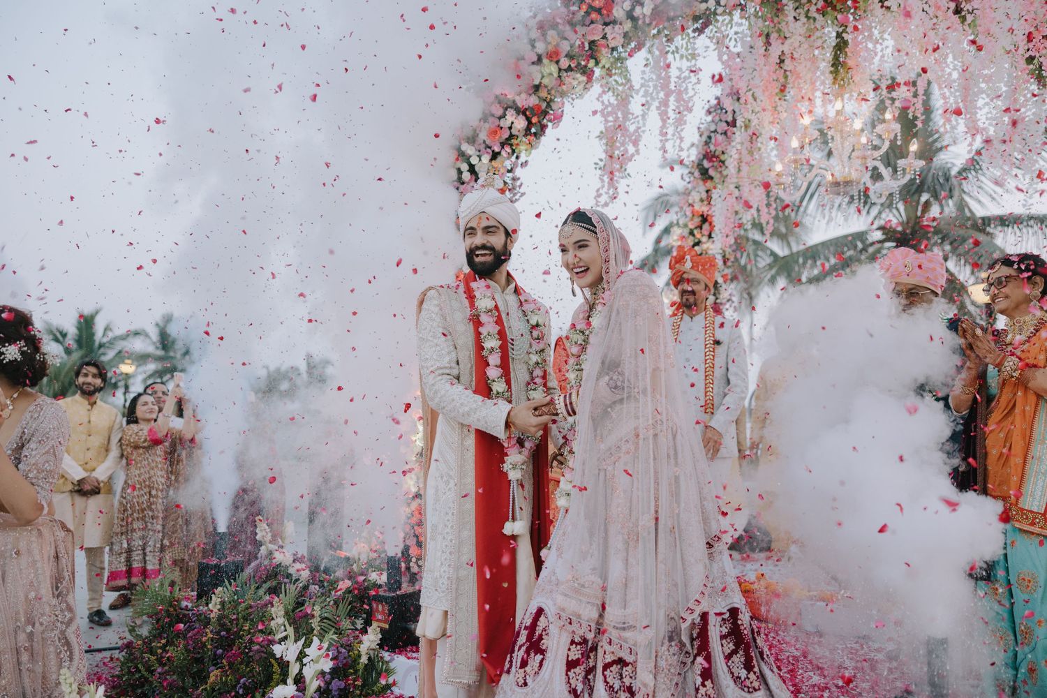 Traditional Indian wedding celebration with rose petal shower and decorative white backdrop.
