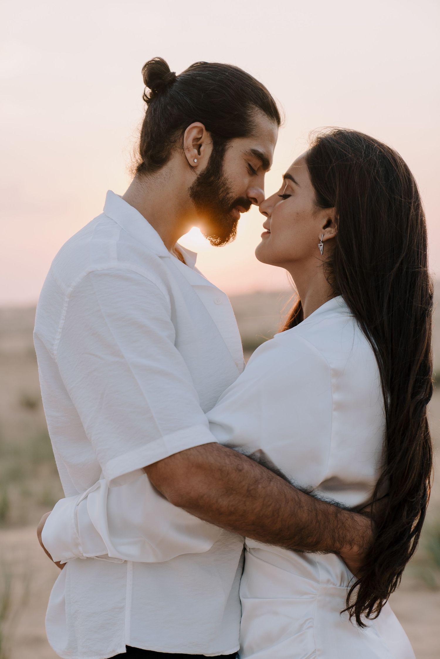 Intimate sunset portrait of couple in white attire sharing a tender moment.