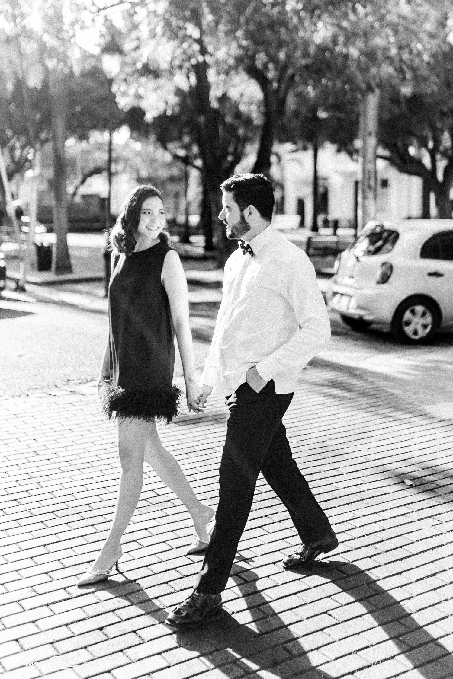 Stylish couple walking hand in hand on a brick sidewalk in black and white.