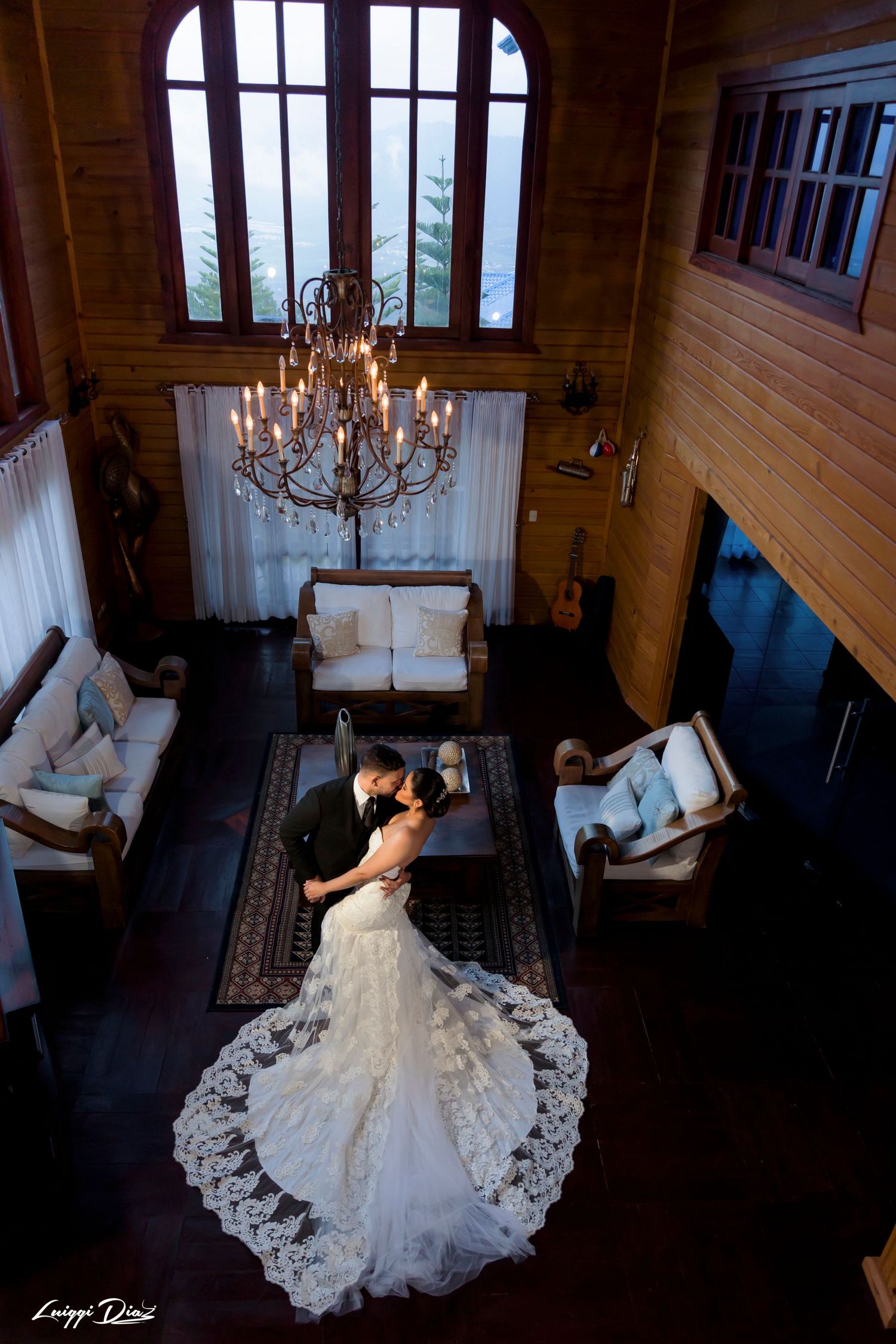 Elegant wedding couple dancing in a rustic wooden lodge under a crystal chandelier.