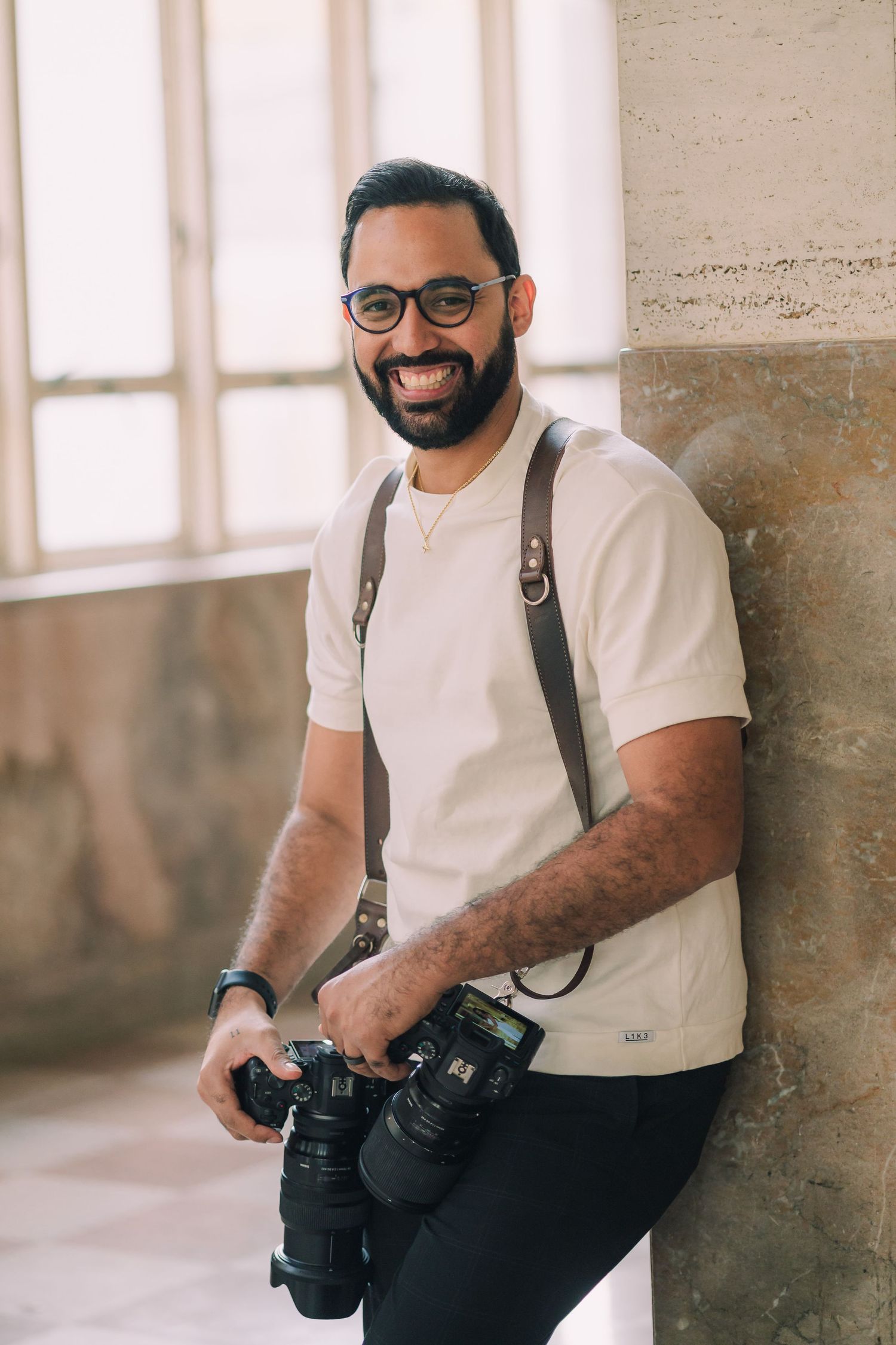 Professional photographer with two cameras wearing white polo and suspenders.