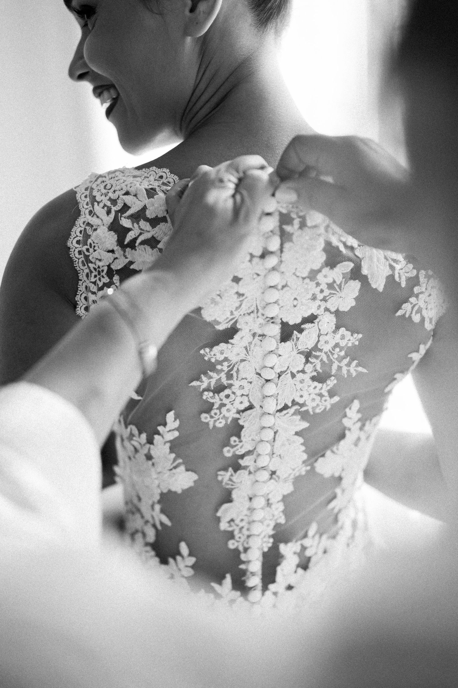 Black and white detail shot of intricate lace wedding dress being buttoned.