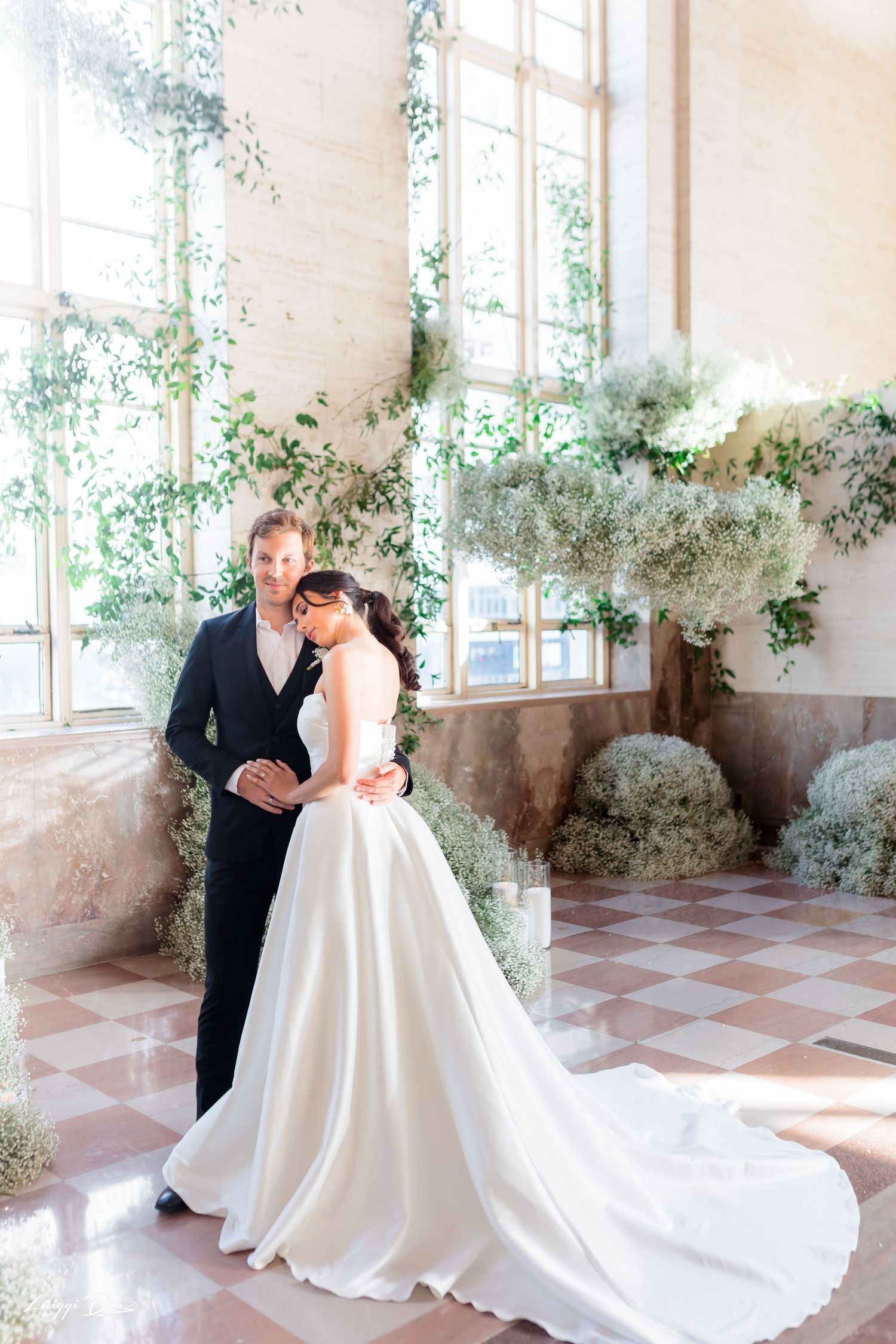Wedding couple poses in a bright room with beautiful floral decor and windows.