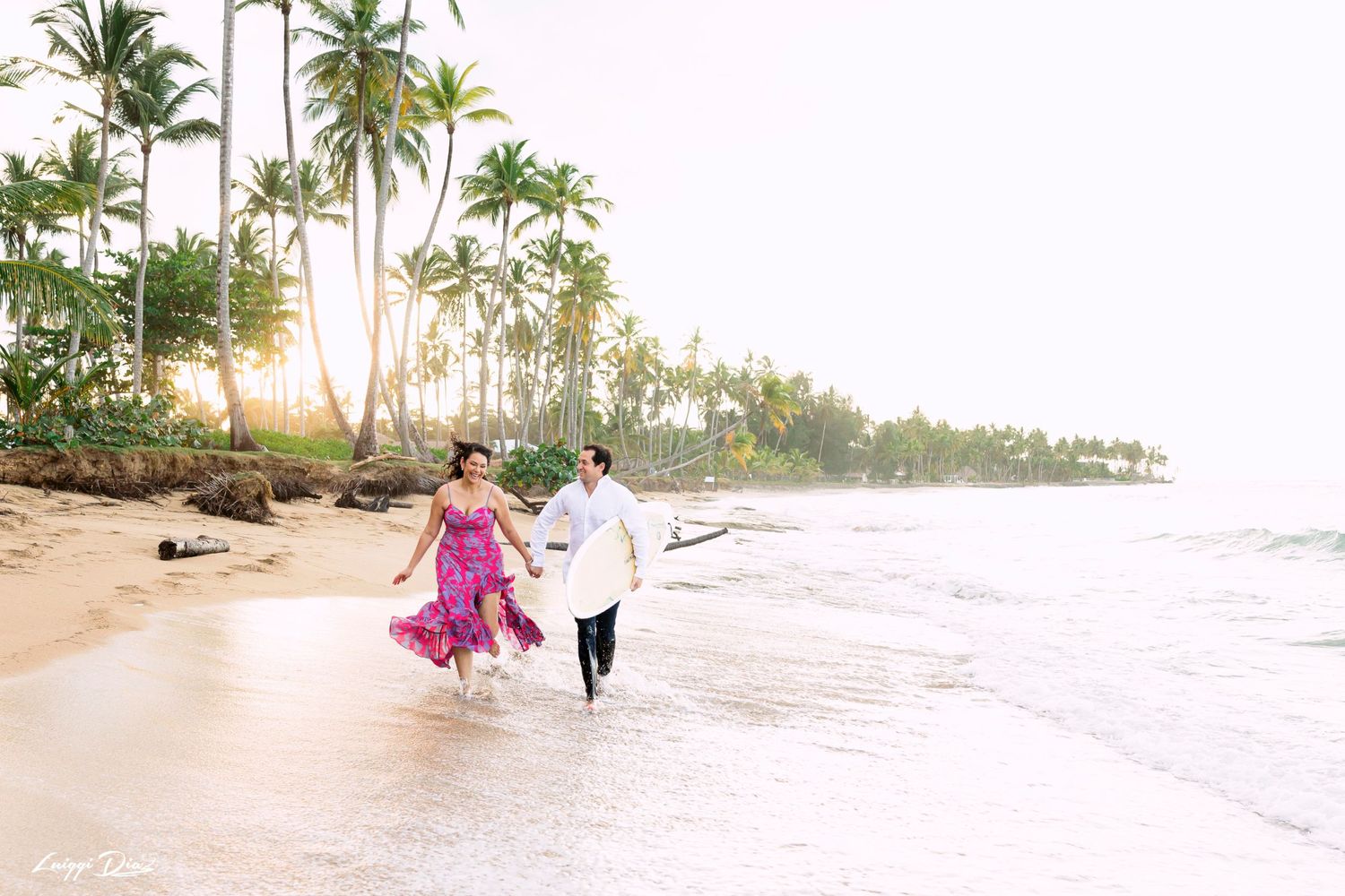 A couple twirls together on a tropical beach at sunset with palm trees in the background.