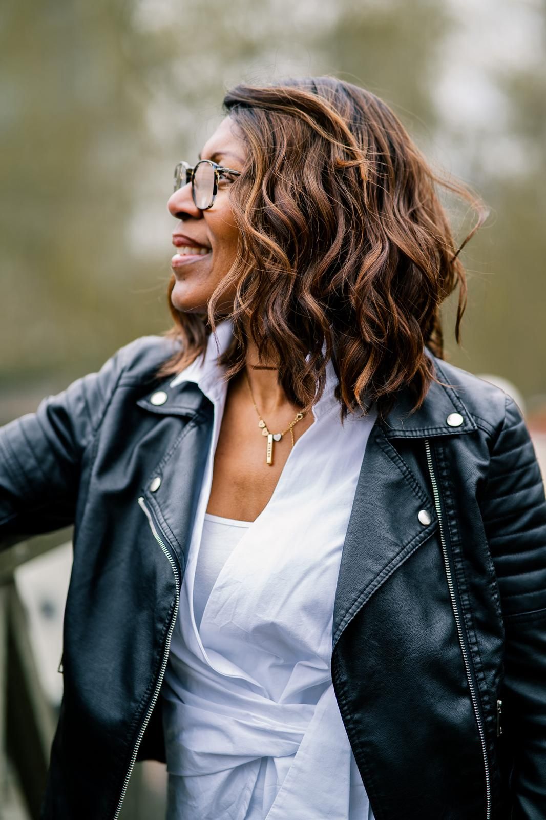 Stylish leather jacket and white top outfit with wavy hair and glasses.