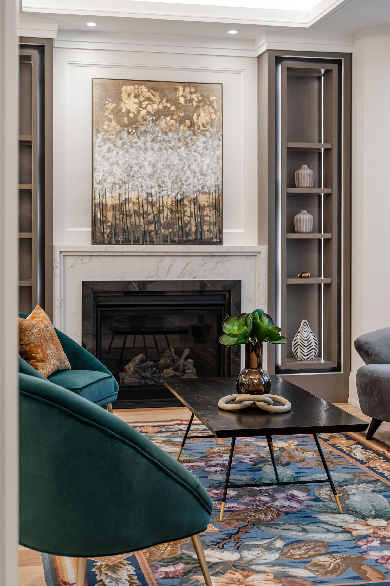 Sophisticated living room with emerald chairs, abstract art, and built-in fireplace with marble surround.
