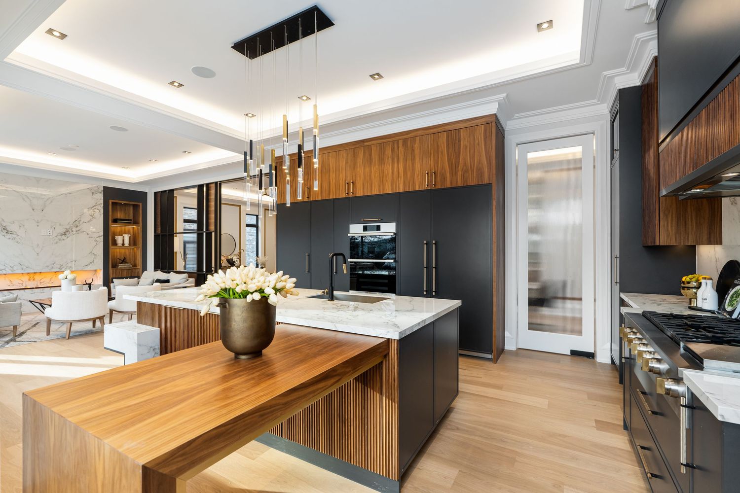 Open concept kitchen with wooden breakfast bar, black appliances, and marble details under tray ceiling.