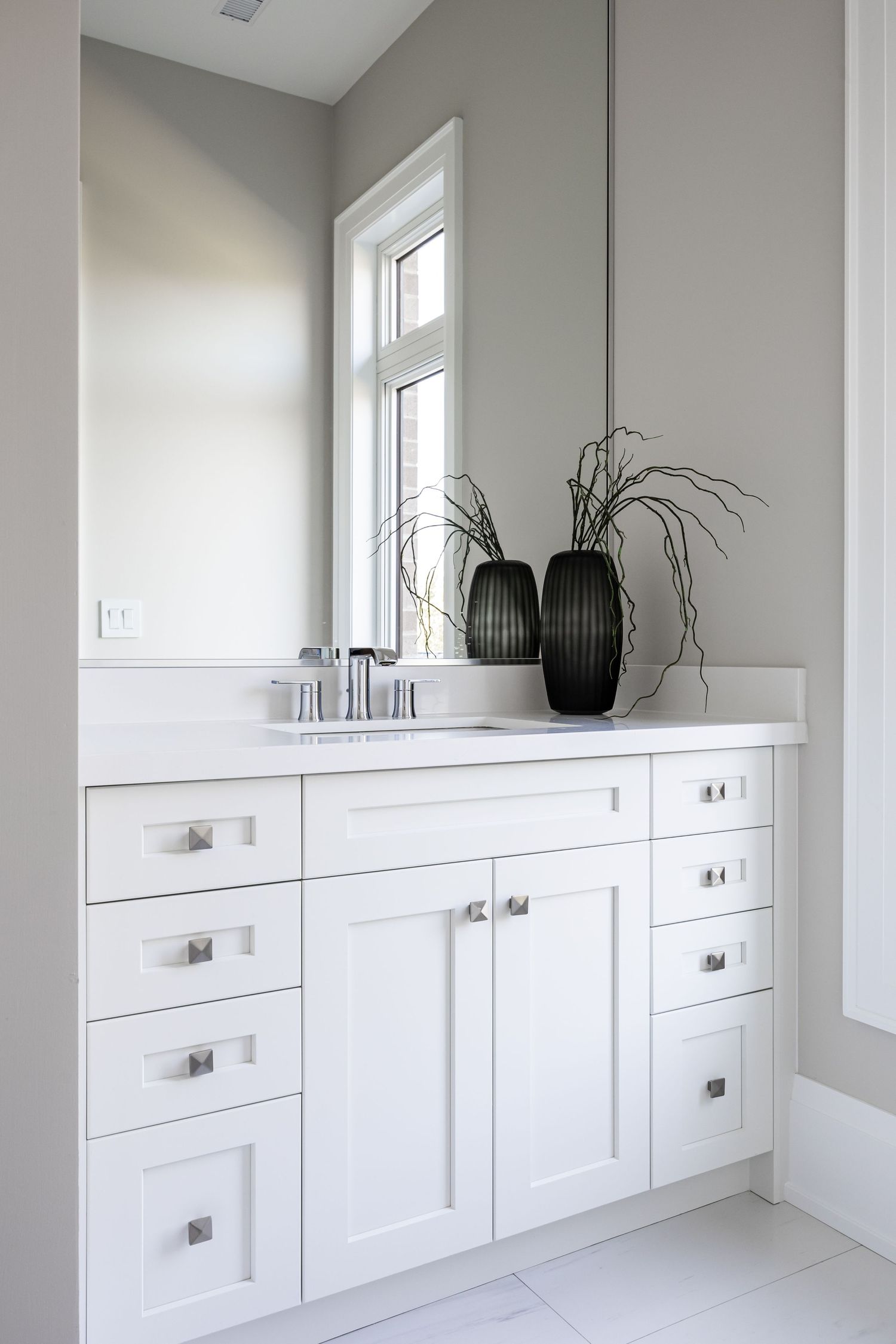 Modern white bathroom vanity with sleek hardware and black decorative vases against a light gray wall.