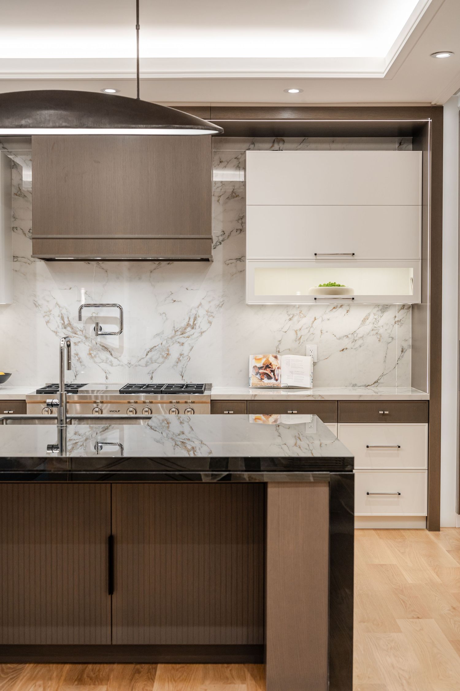 Luxury kitchen featuring marble backsplash, stainless appliances, and dark island with pendant lighting.