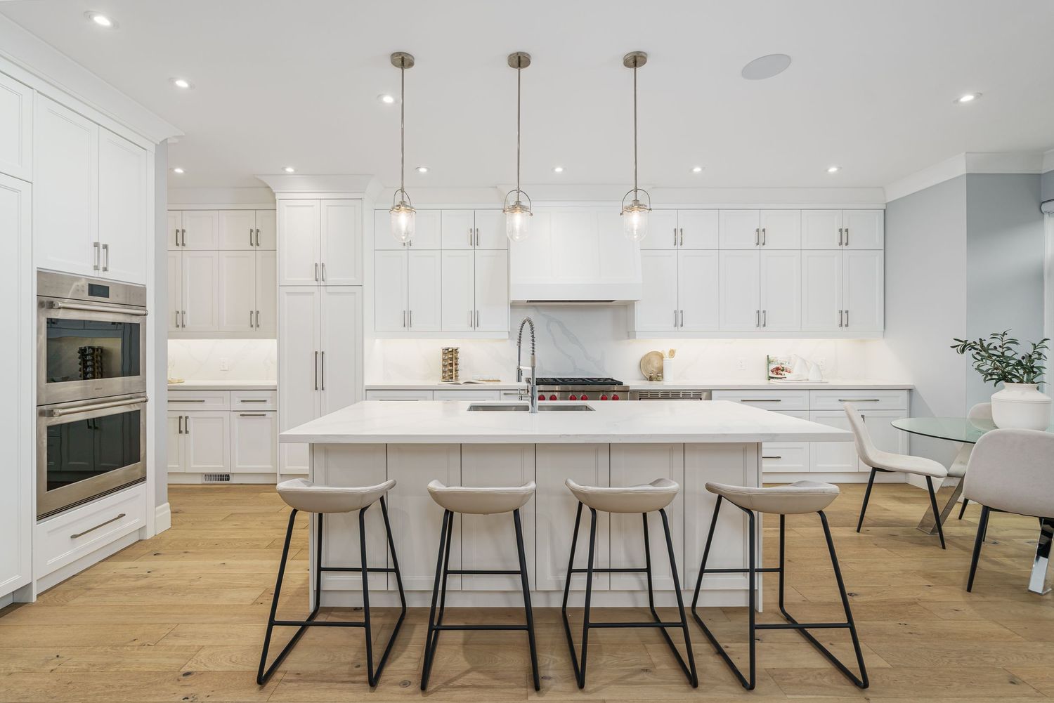 Modern white kitchen with marble countertops, pendant lights, wood floors and contemporary bar stools at large island.