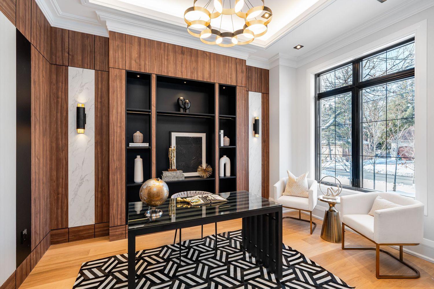 Living room with wood accent wall, geometric black and white rug, and circular chandelier.