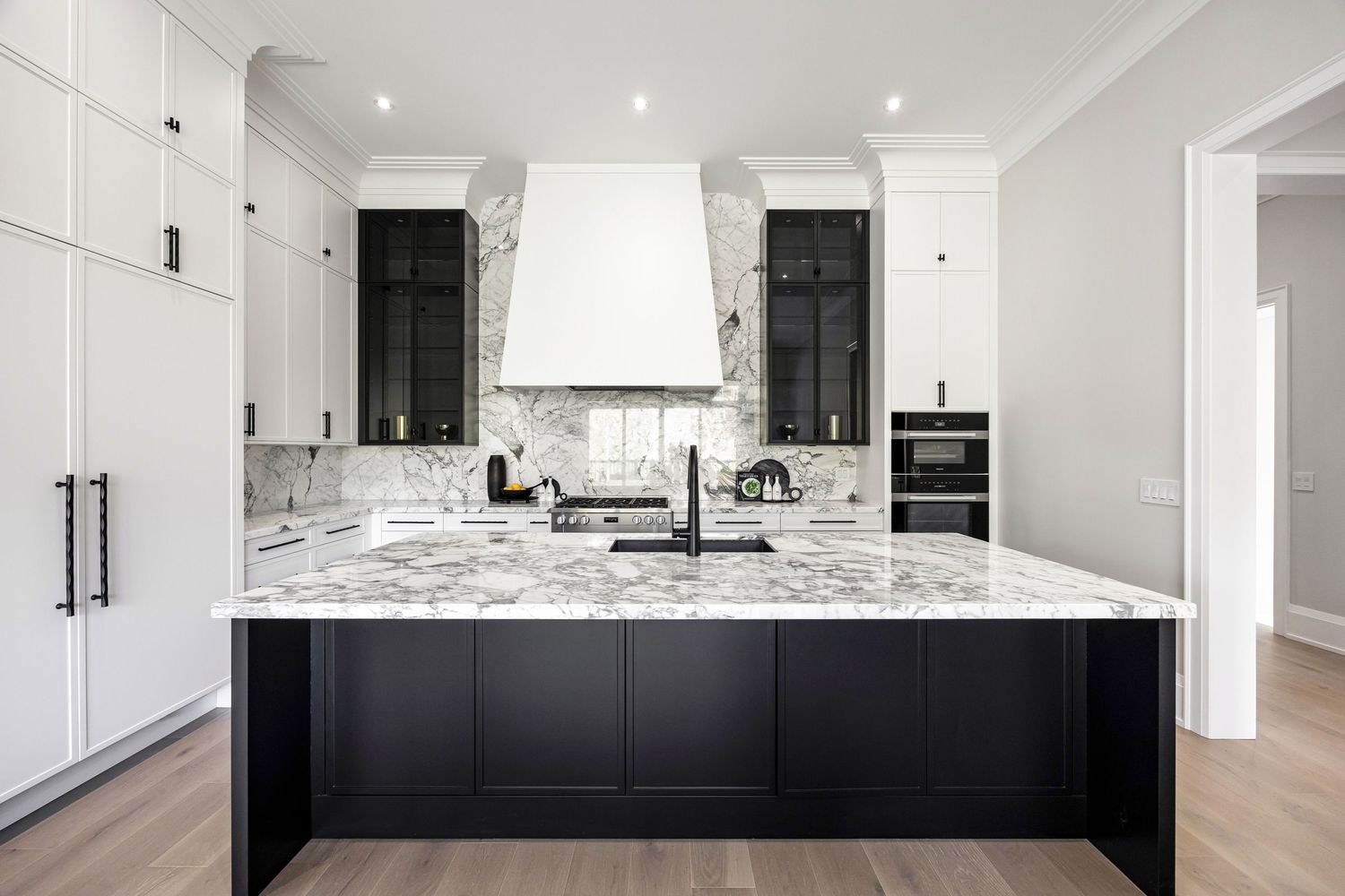 Modern black and white kitchen featuring marble countertops, black cabinetry, and a custom range hood with white walls.