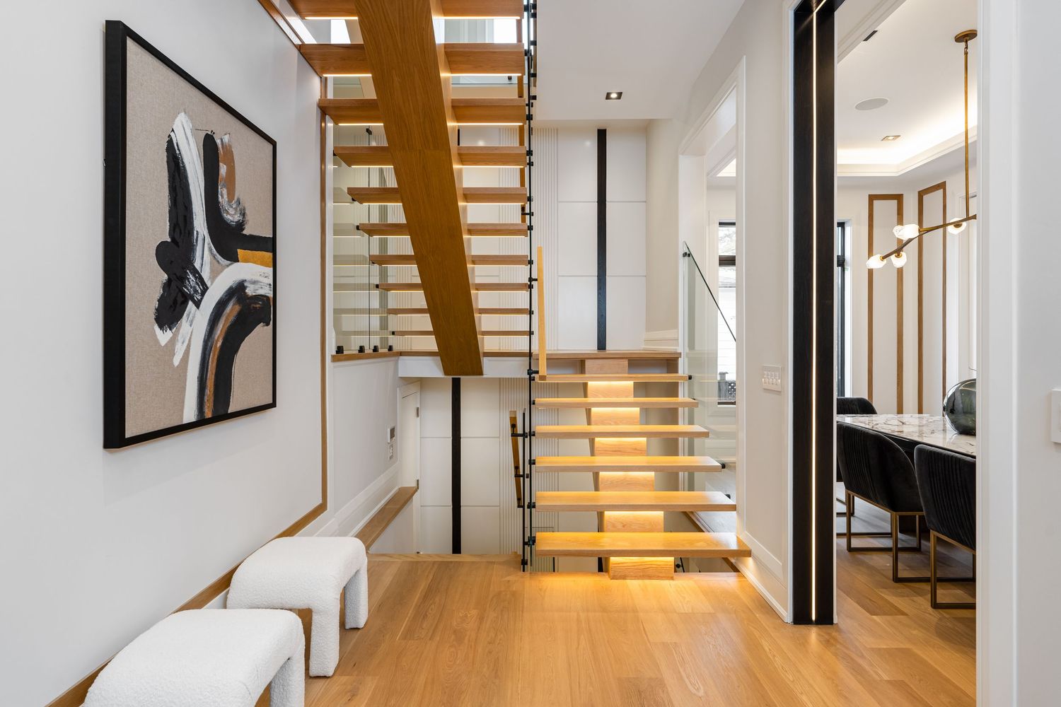 Elegant hallway featuring floating wooden stairs with glass railings and warm LED lighting.