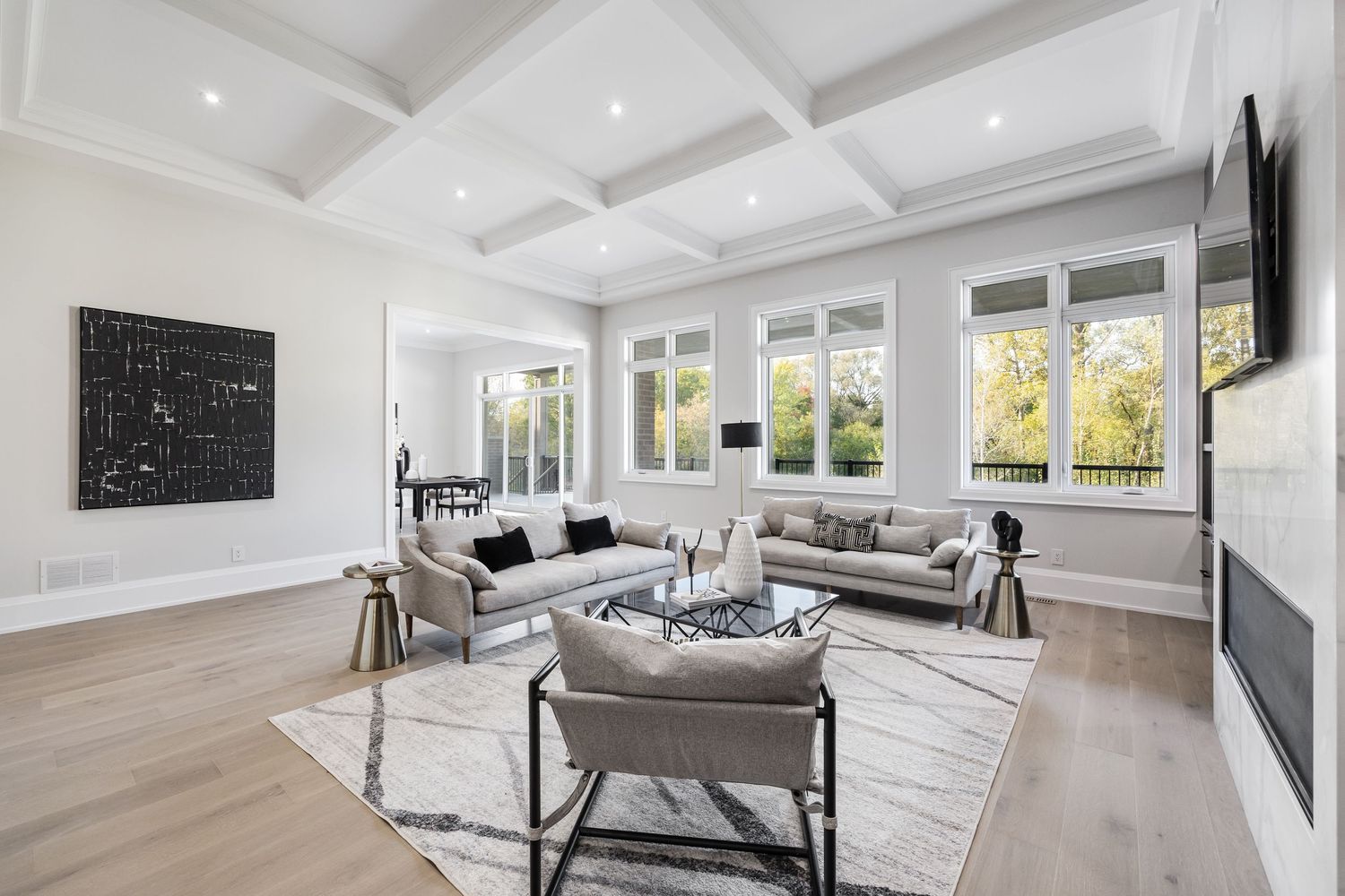 Contemporary living room with coffered ceiling, abstract art, and light gray furniture on hardwood floors.