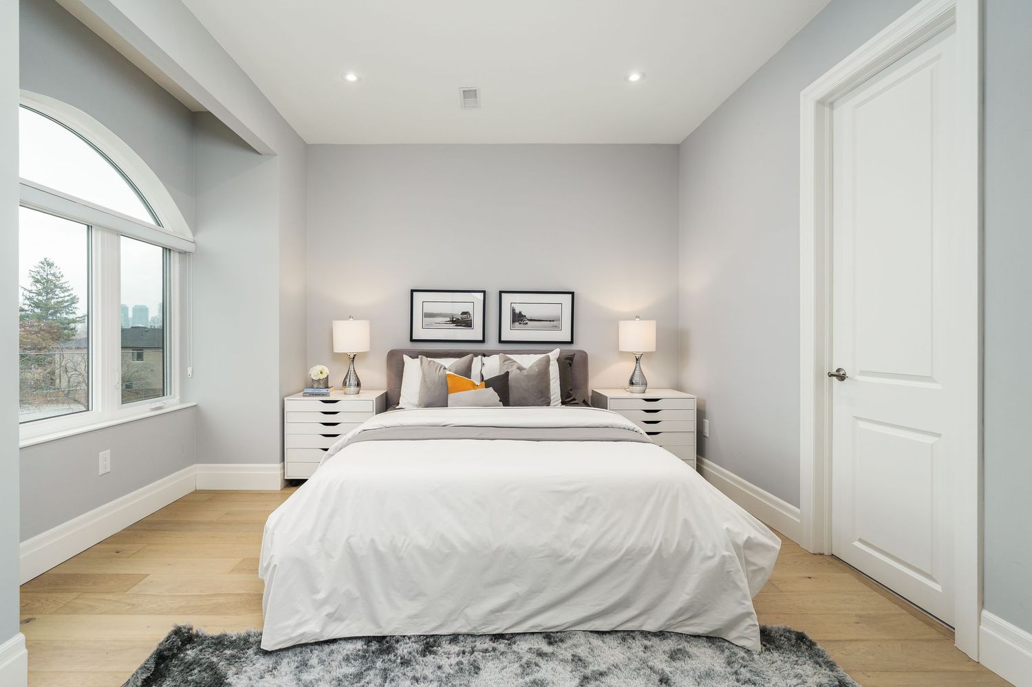 Interior view of modern bedroom with white linens, hardwood floors, and recessed lighting showing luxurious finishes.