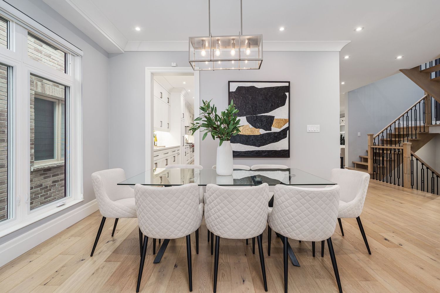 Contemporary open concept dining space with crystal chandelier, white tufted chairs and light hardwood floors.