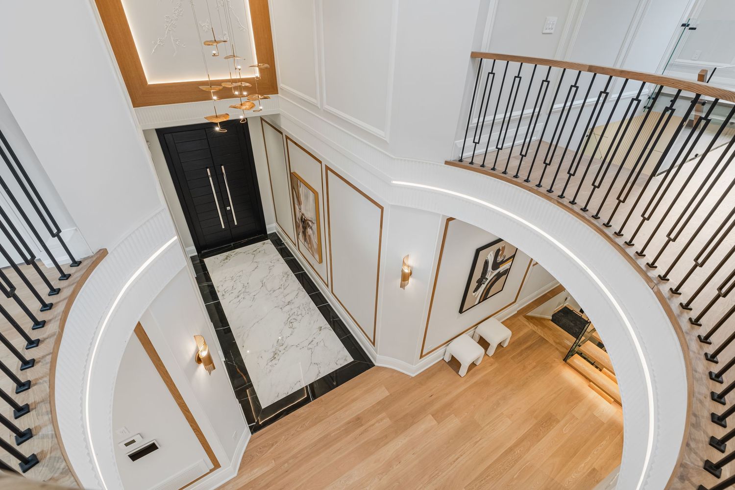Grand entrance foyer with curved staircase, white paneled walls, and black double doors.