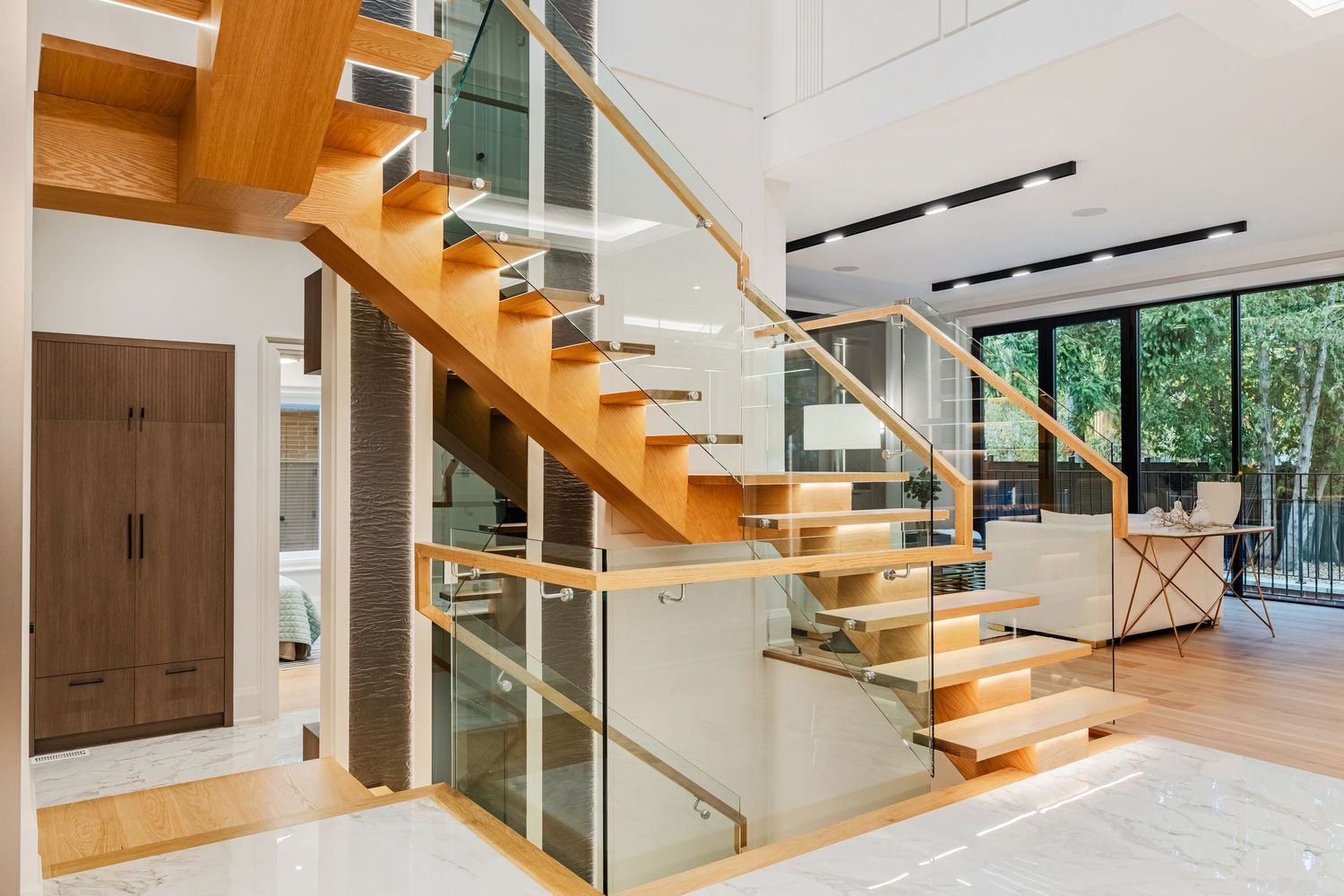 Floating wooden staircase with glass railings and natural light streaming through windows.
