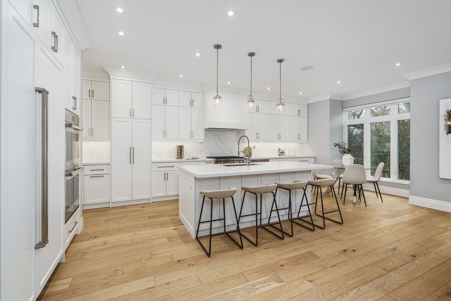 Modern white kitchen with hardwood floors, pendant lights, and island with bar stools in an open concept design.