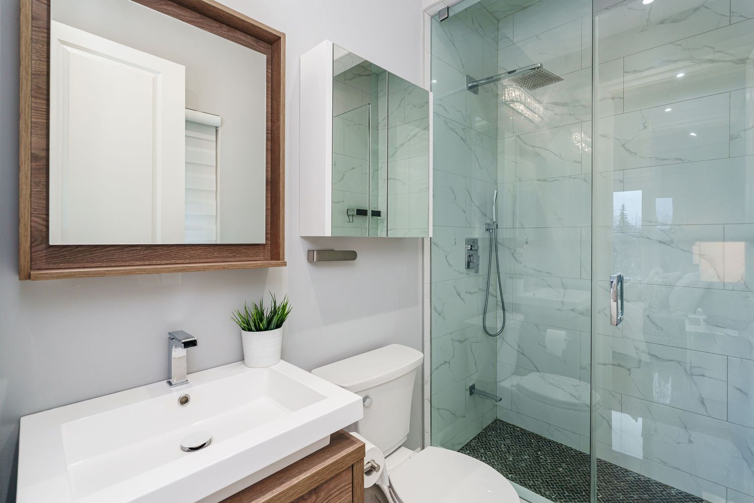 Modern luxury bathroom with glass shower enclosure, grey tile walls, and floating vanity in natural wood tones.