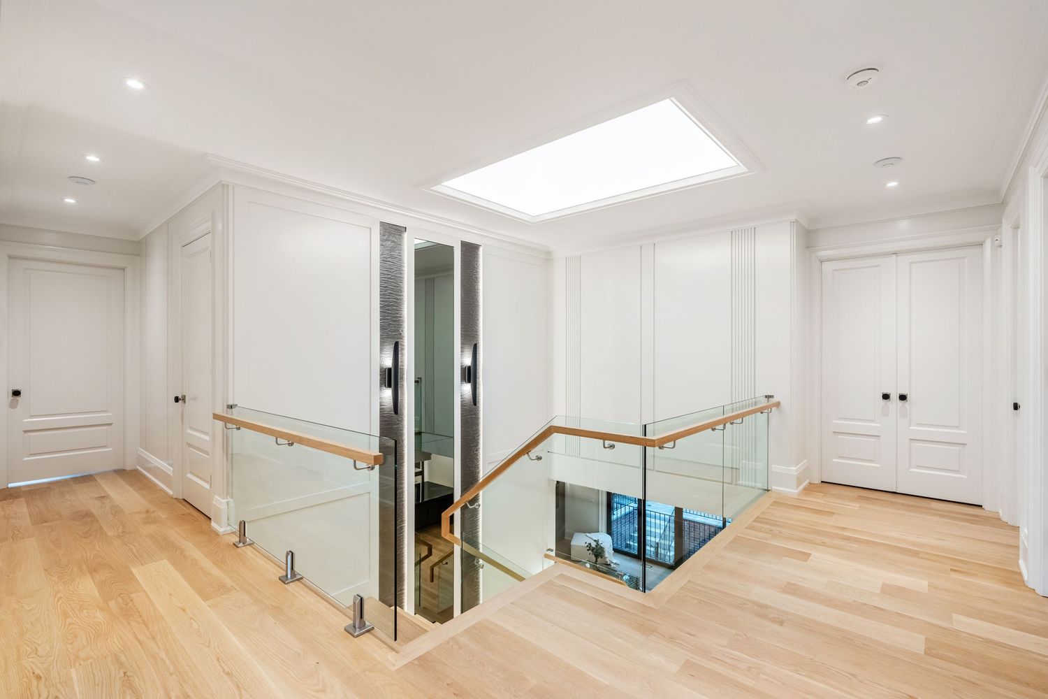 Modern white hallway with glass railing, wooden floors, and skylight featuring built-in storage closets.
