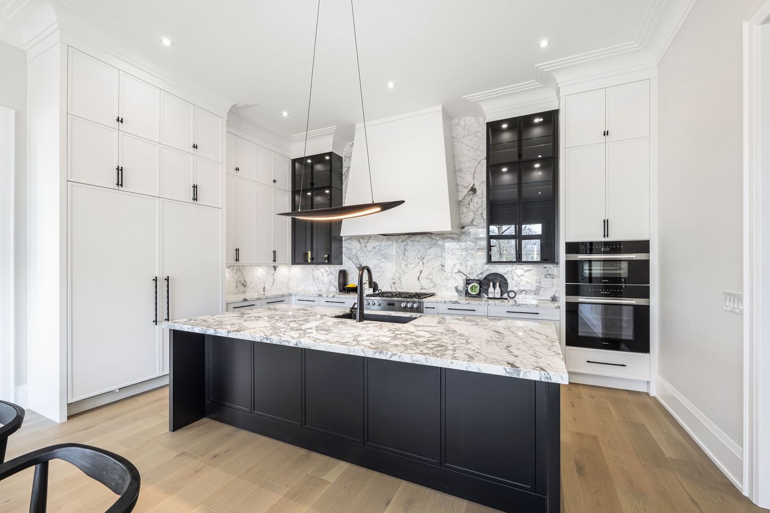 Modern kitchen with black base cabinets, white upper cabinets, marble countertops and light hardwood flooring.