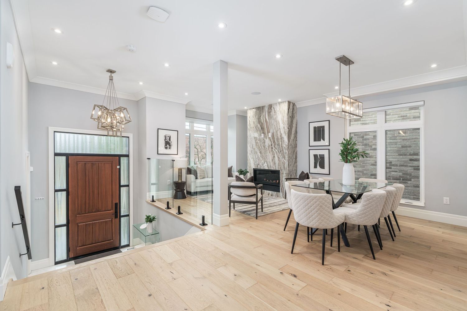 Modern open concept home interior with light hardwood floors, white walls and elegant dining area featuring pendant lighting.