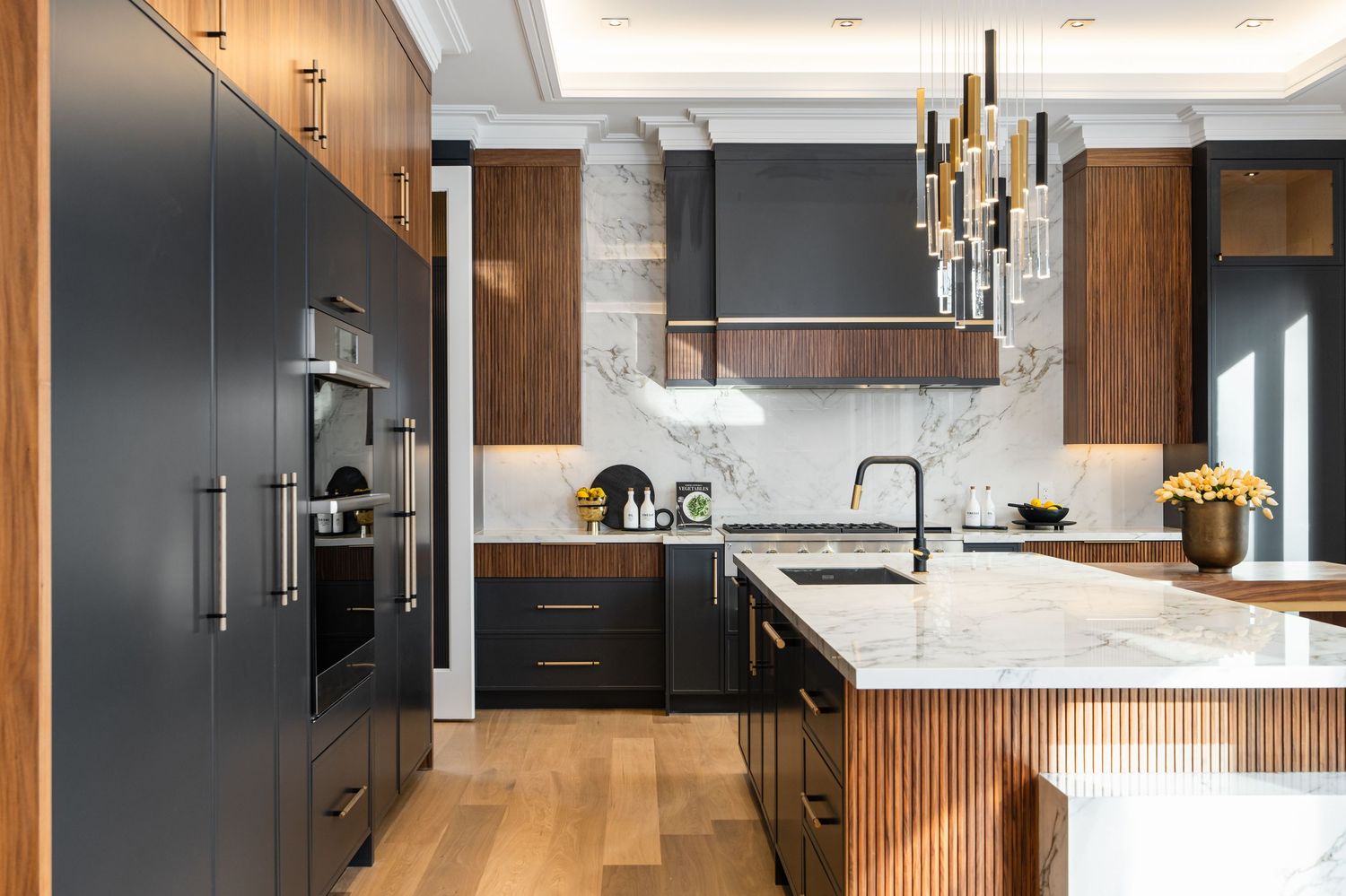 Luxury kitchen featuring black appliances, marble backsplash, and wood paneling with modern pendant lights.