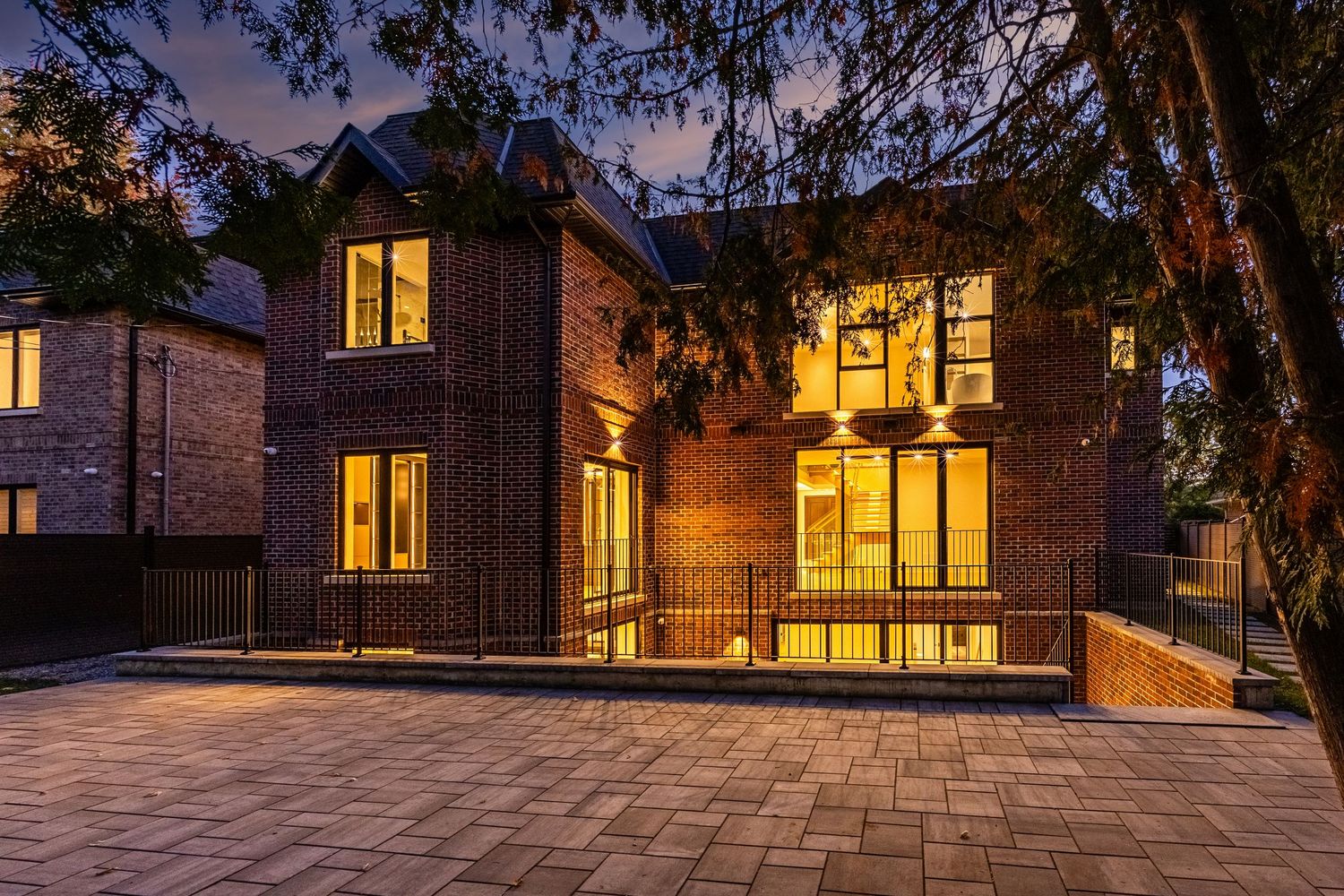 Contemporary brick house with large windows glowing warmly at night.