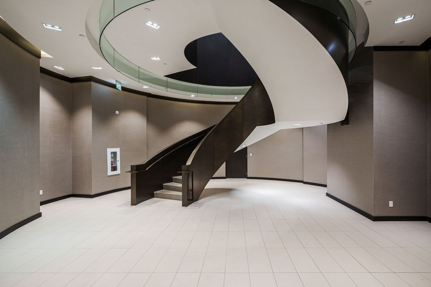 Modern spiral staircase with black railing curves dramatically in a minimalist interior with light floors and recessed lighting.