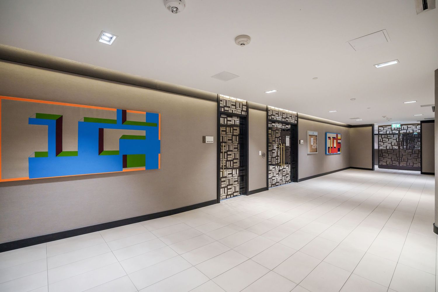 Long hallway with fluorescent lighting and multicolored geometric wall designs stretches through a modern commercial building.
