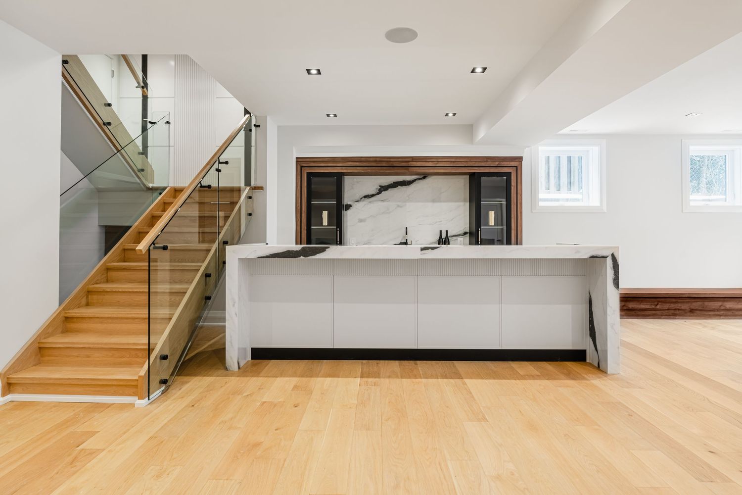 Contemporary open concept kitchen with wooden stairs and glass railings in a bright interior space.