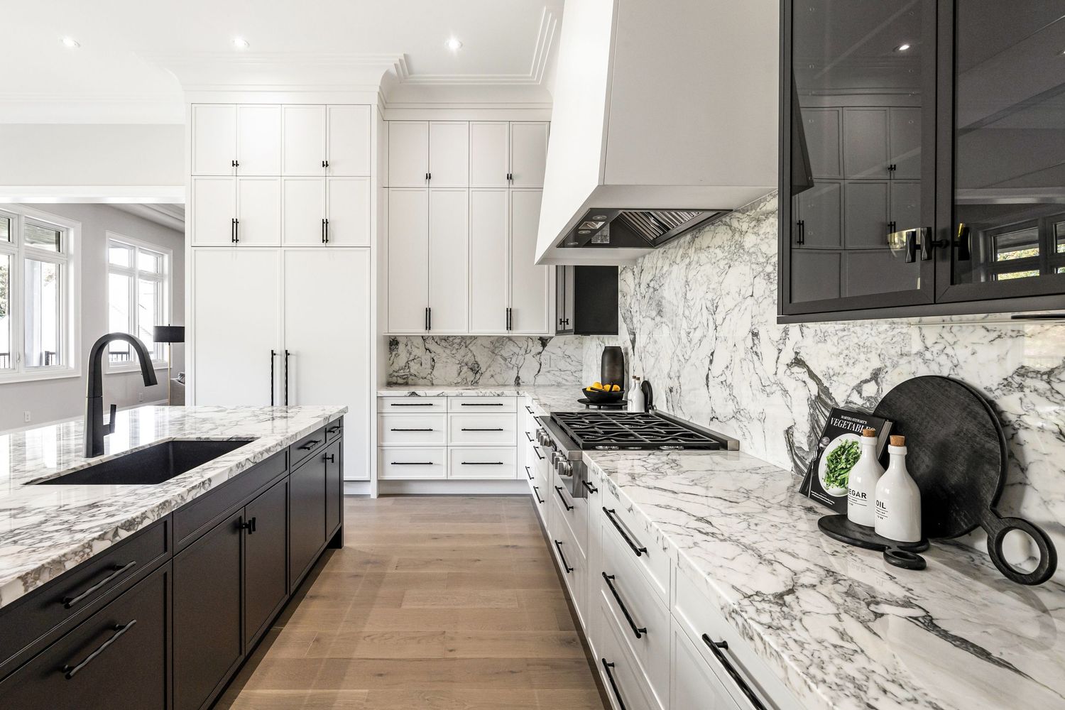 Modern kitchen with white marble countertops, dark lower cabinets, white upper cabinets, and hardwood flooring.