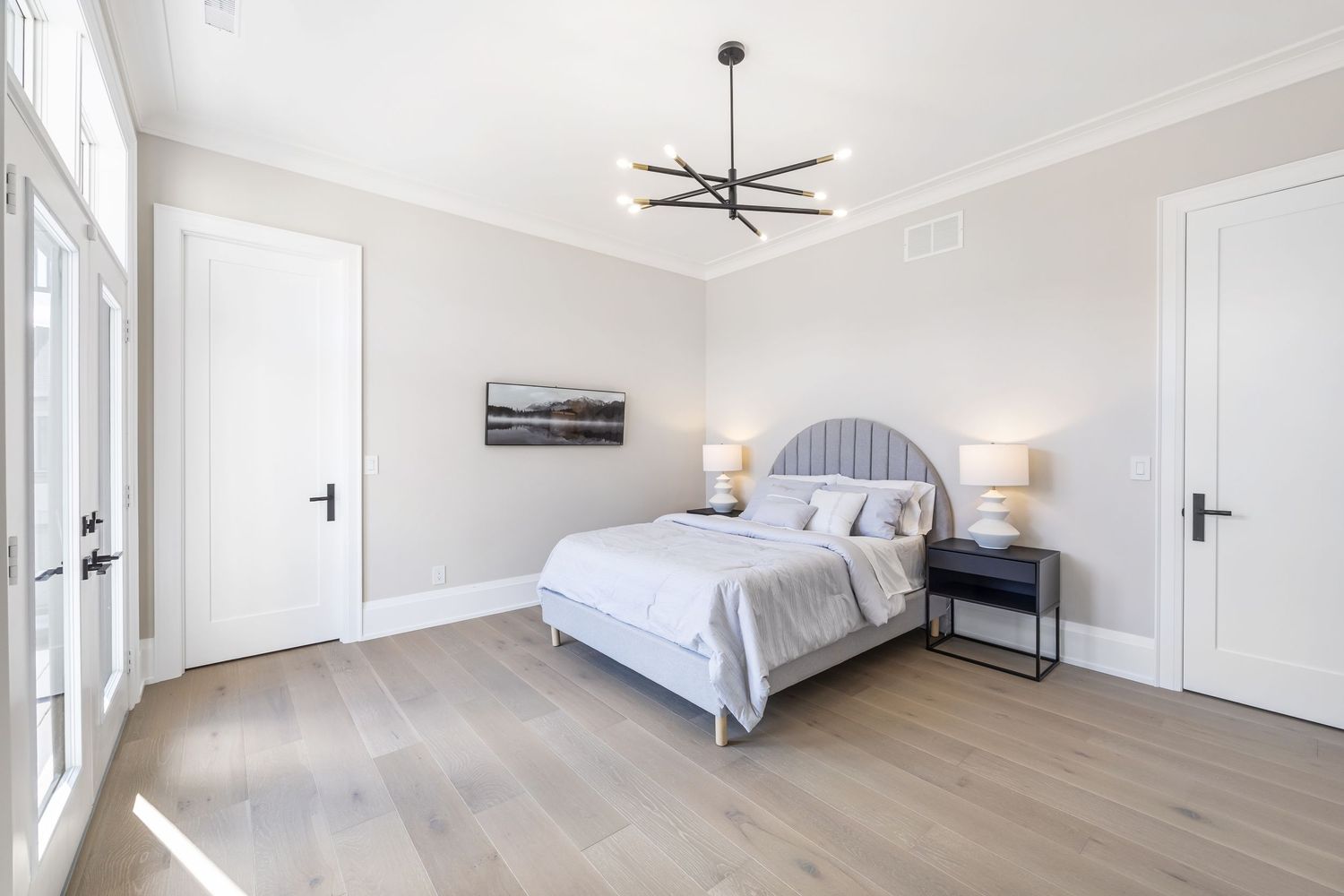 Contemporary bedroom with gray upholstered headboard, black ceiling fan, and French doors leading outside.