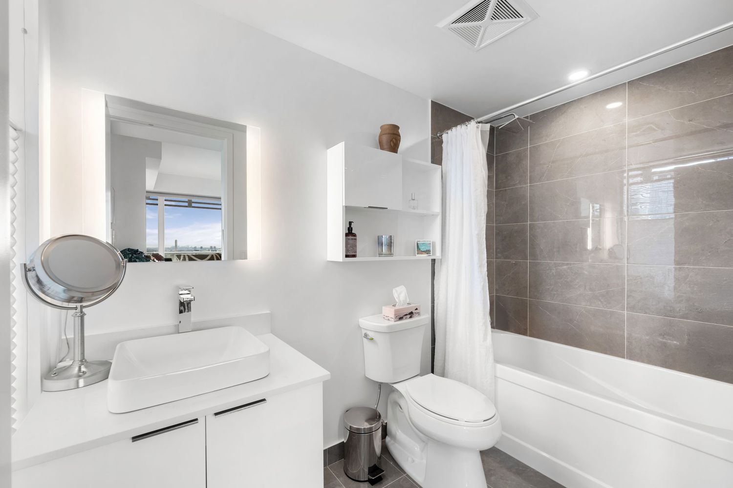 Modern bathroom interior with grey tile walls, white fixtures, and pendant lighting showcases sleek minimalist design.