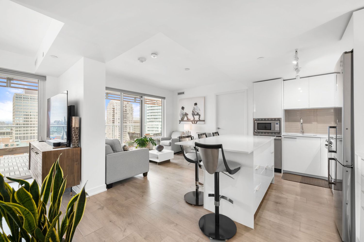 Modern open concept condo with white kitchen, living area, and city views through large windows.