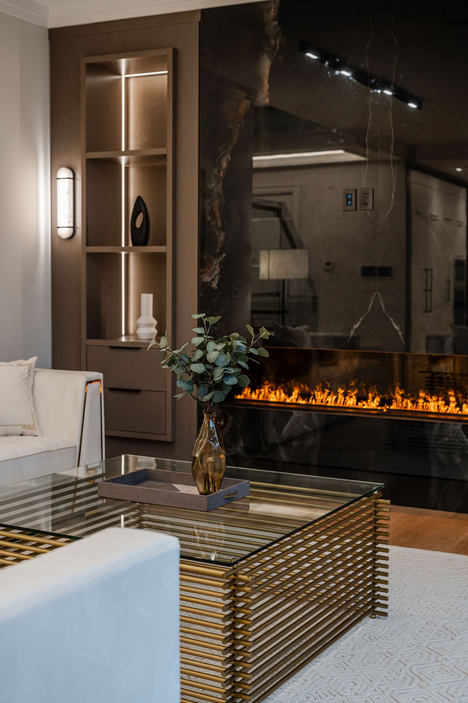 Modern living room with gold metal coffee table, linear fireplace, and illuminated built-in shelving.