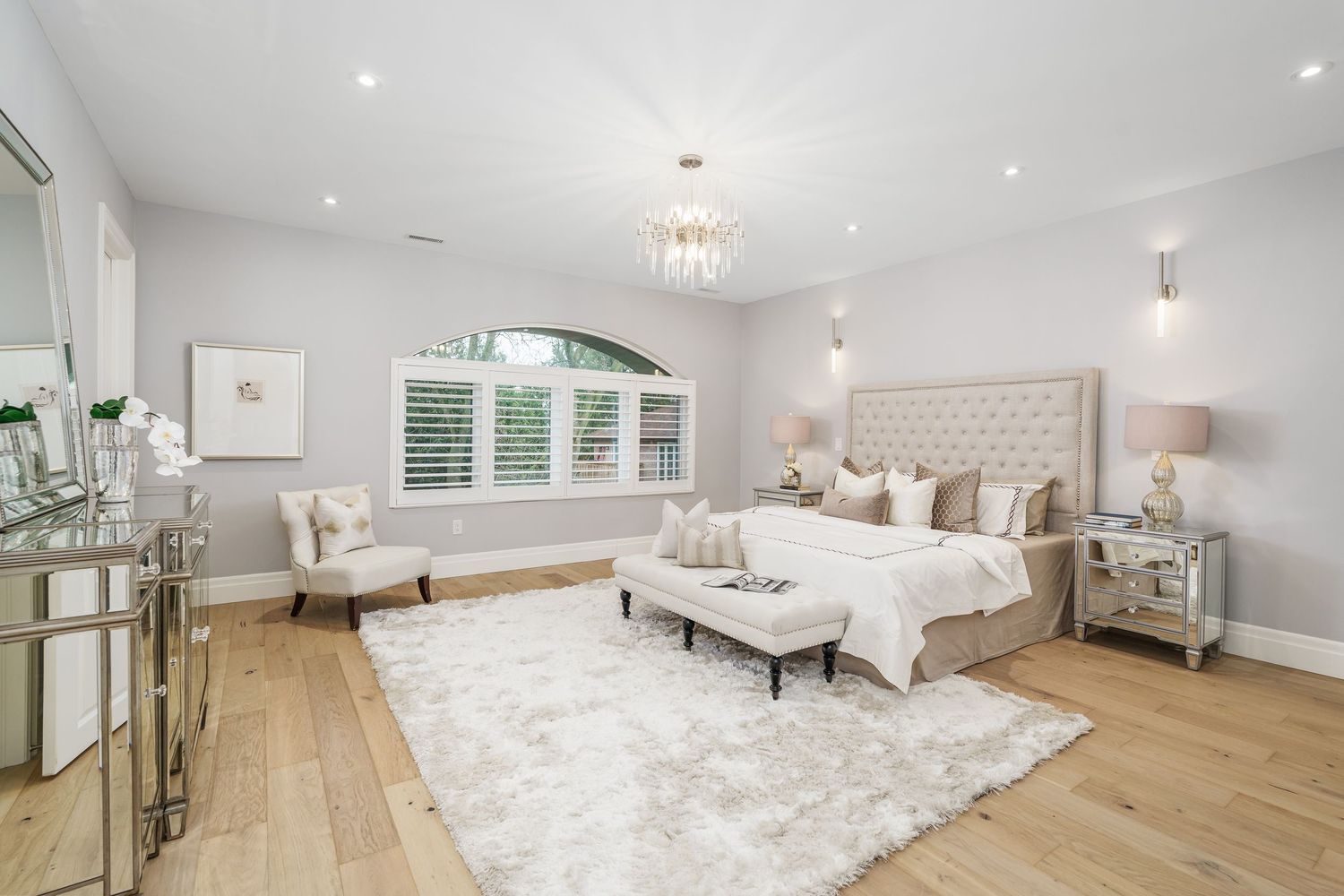 Spacious master bedroom with white finishes features tufted headboard, recessed lighting, and natural oak hardwood floors.