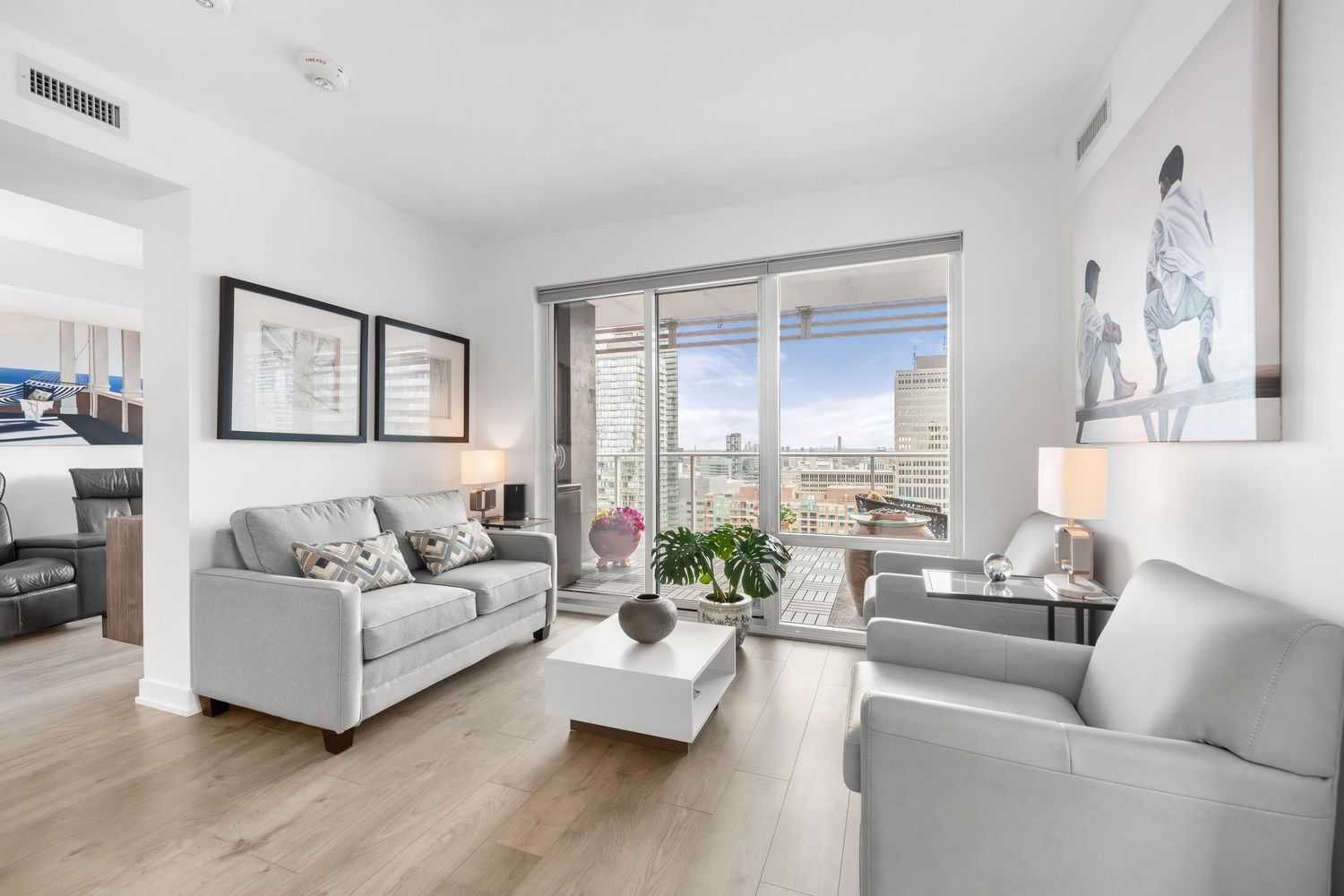 luxury condo living room with light grey furniture, hardwood floors and floor-to-ceiling windows overlooking city views.