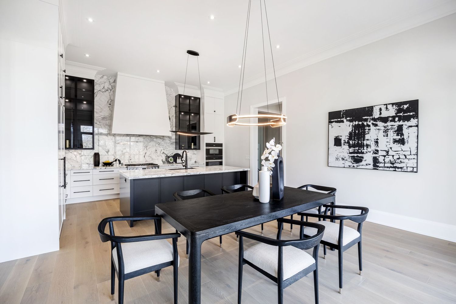 Sleek dining area with black table and chairs adjacent to white and marble kitchen.